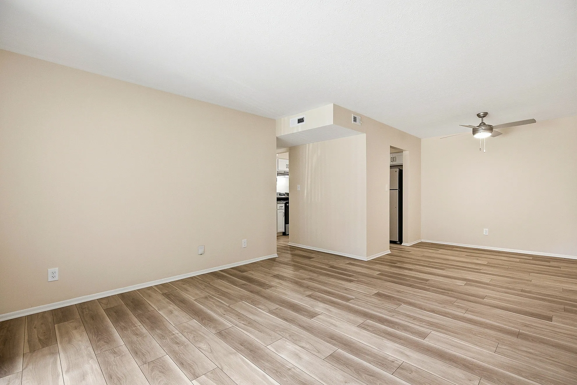 Bright, open living area with modern wood flooring and sleek ceiling fan, flowing into a contemporary kitchen space.