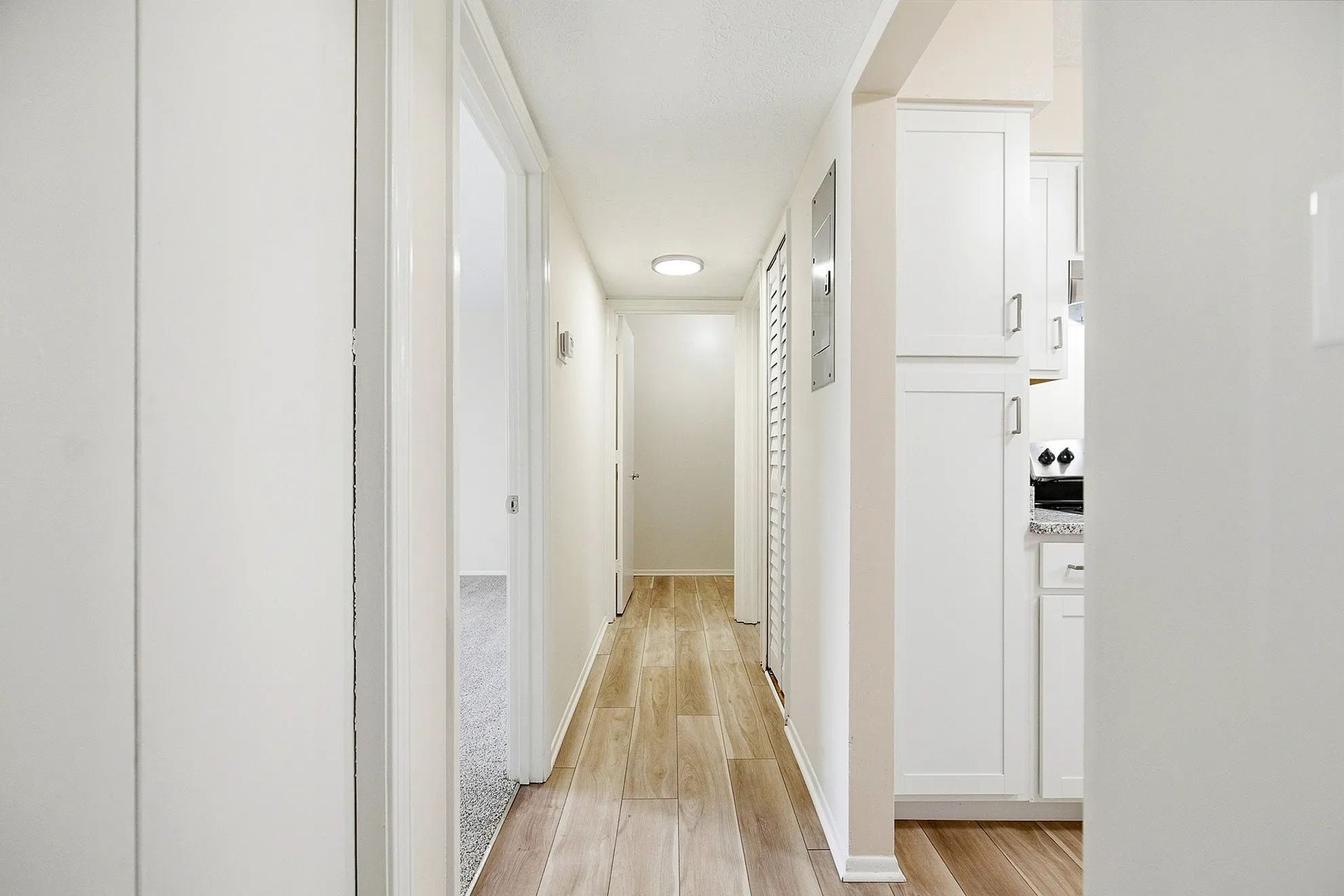 Bright, modern hallway with elegant wood flooring leading to a cozy kitchen and bedrooms.