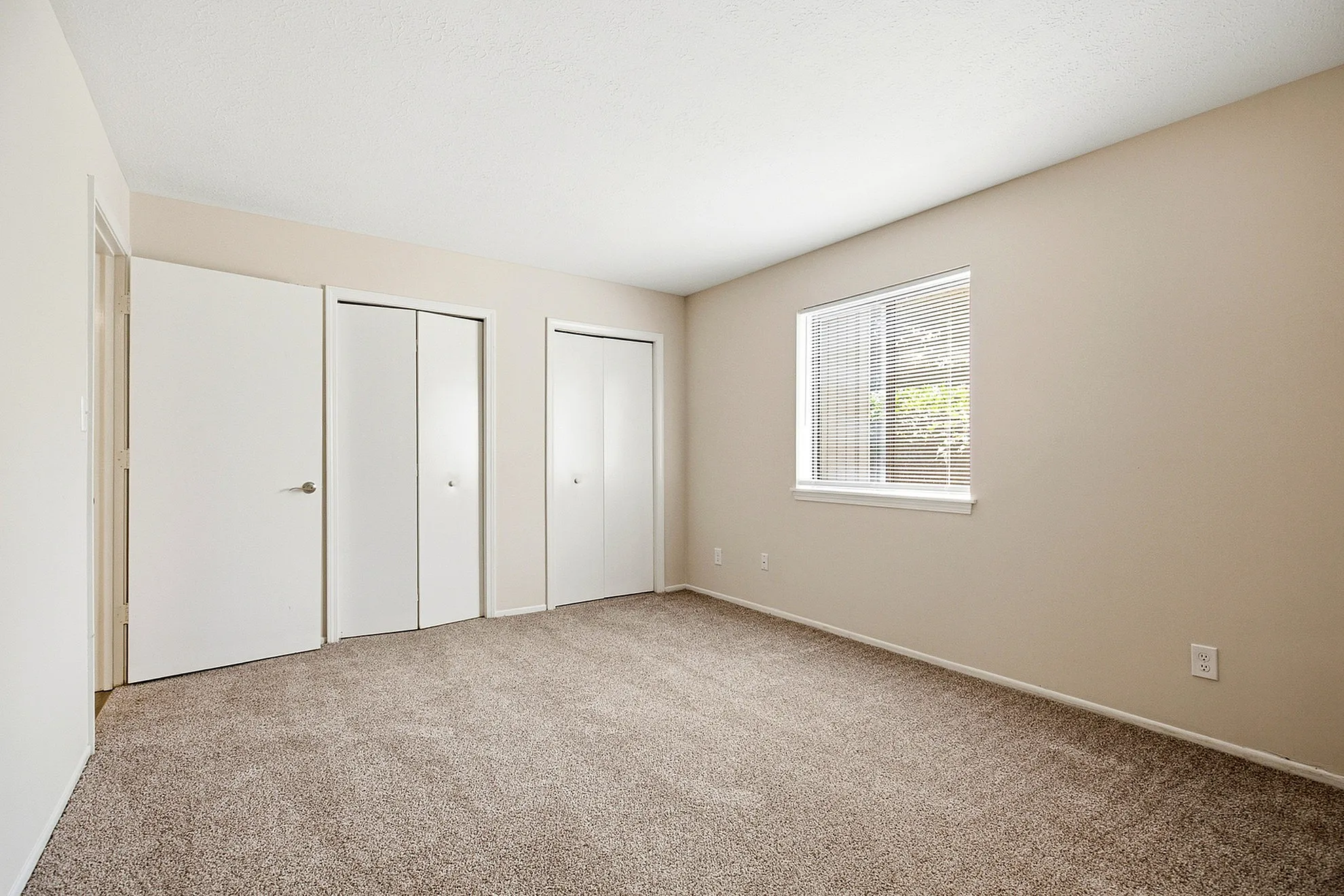 Bright and spacious bedroom with plush carpet, ample closet space, and large window for natural light.