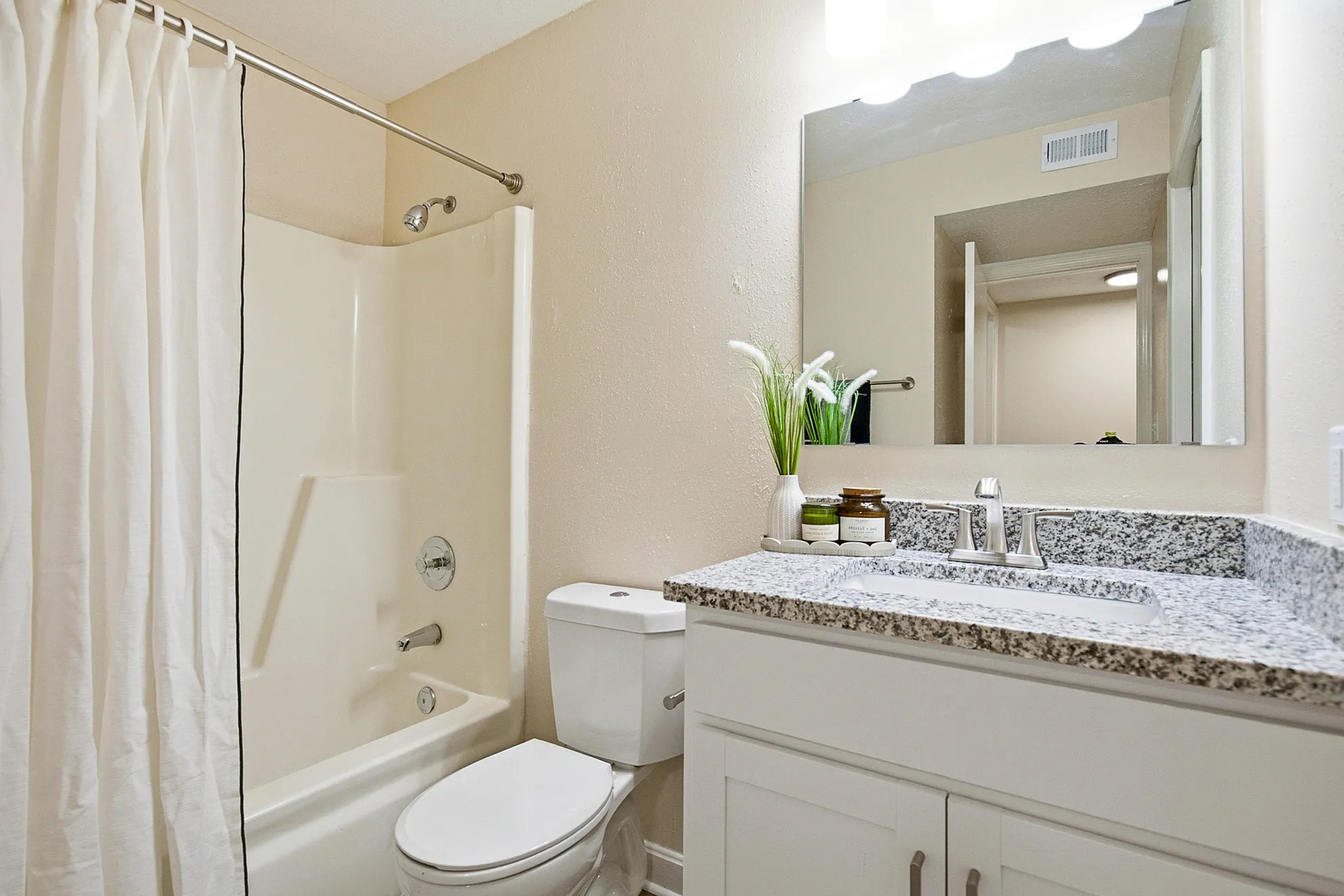 Elegant bathroom featuring a modern granite countertop, stylish white cabinetry, polished fixtures, and a spacious bathtub with a chic shower curtain.