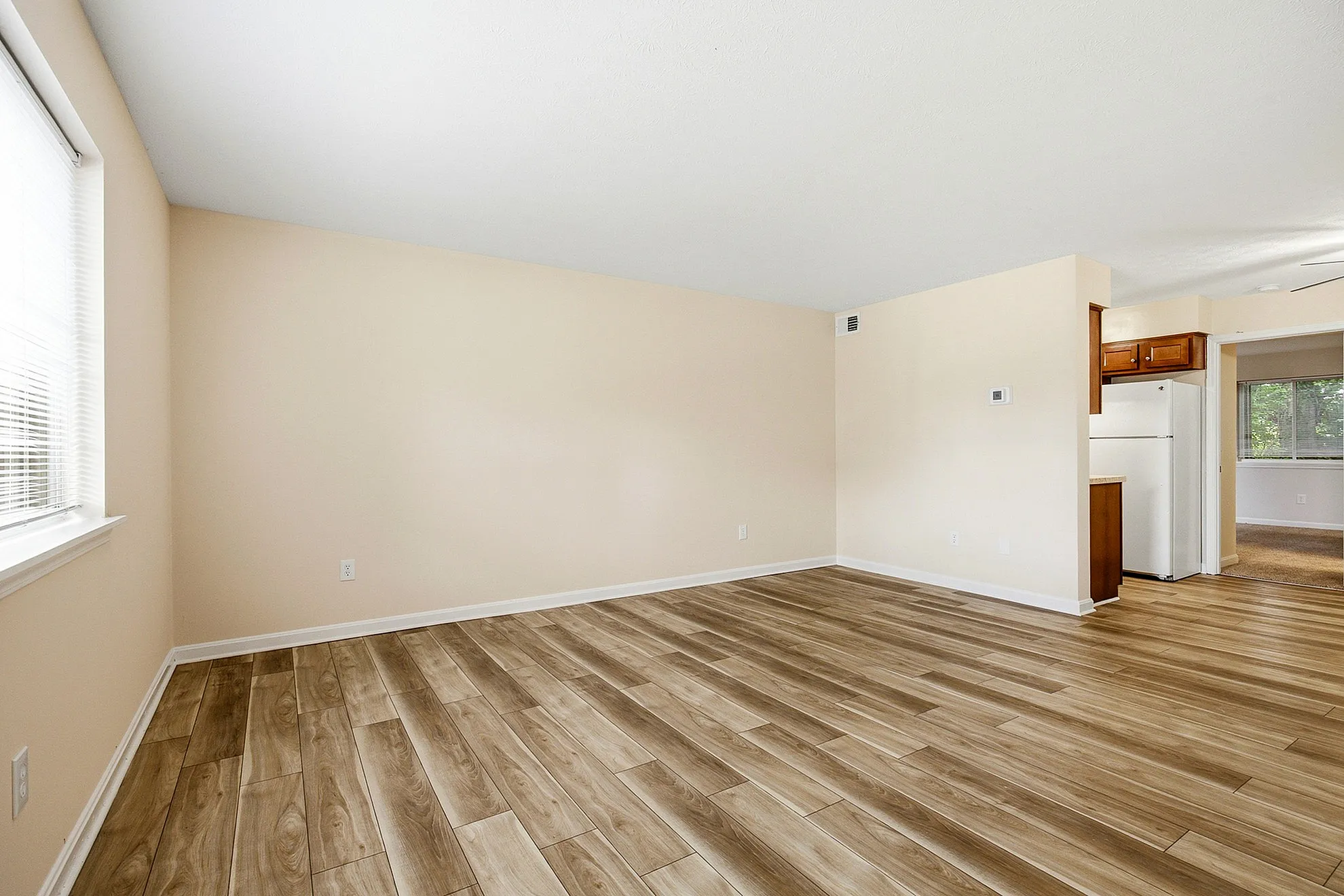 Bright and inviting living area with hardwood floors and neutral walls, leading to a cozy kitchen space with modern appliances.