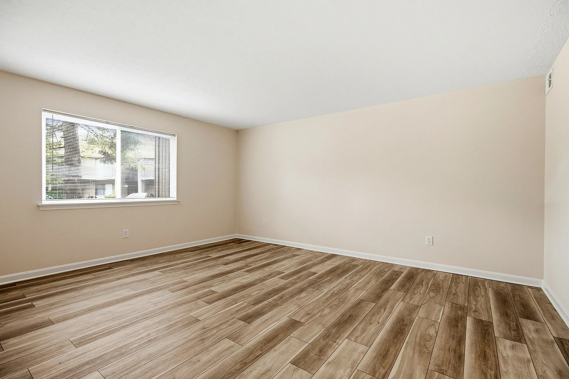 Bright, spacious room with elegant wooden flooring and a large window inviting natural light.