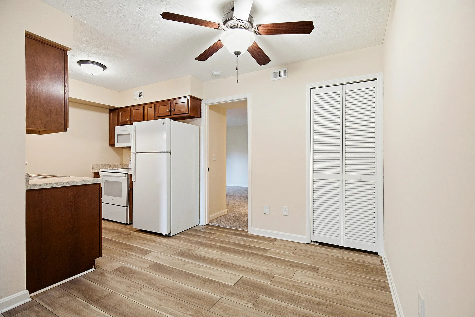 Inviting kitchen area featuring modern appliances, elegant wood cabinetry, and sleek laminate flooring under a bright ceiling fan.