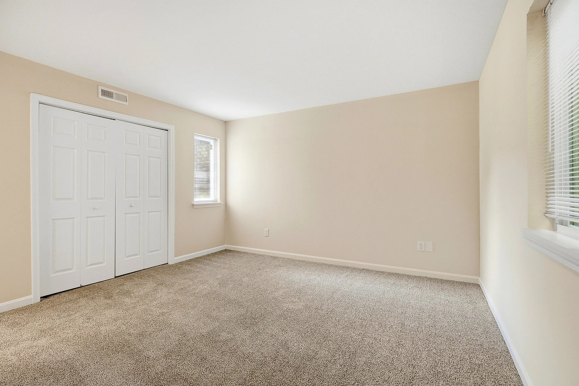Bright and spacious carpeted room with large windows and a sleek white closet, perfect for a cozy and inviting bedroom setting.