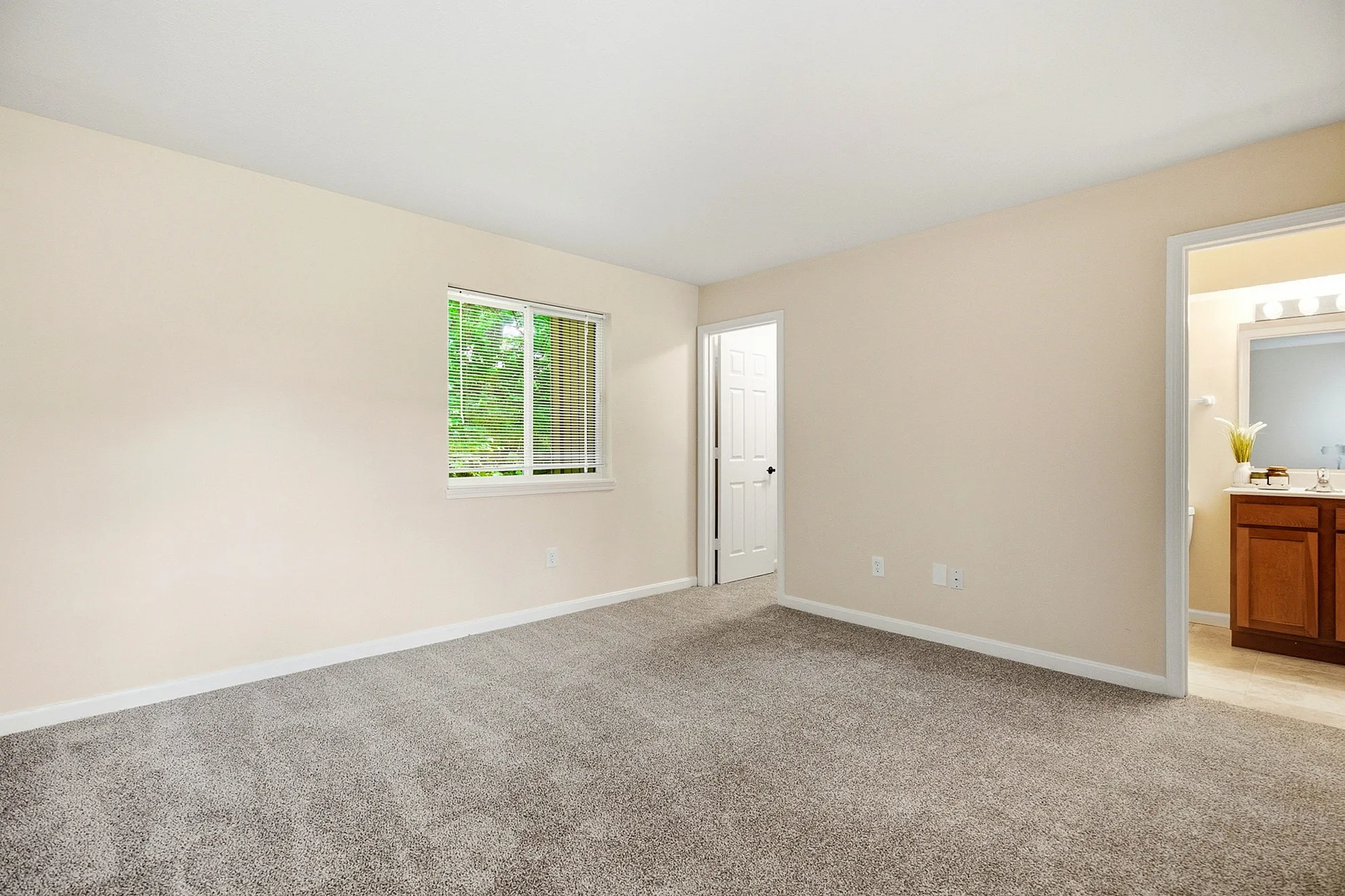 Spacious bedroom with plush carpet, large window offering natural light, and direct access to an elegant bathroom with modern fixtures.