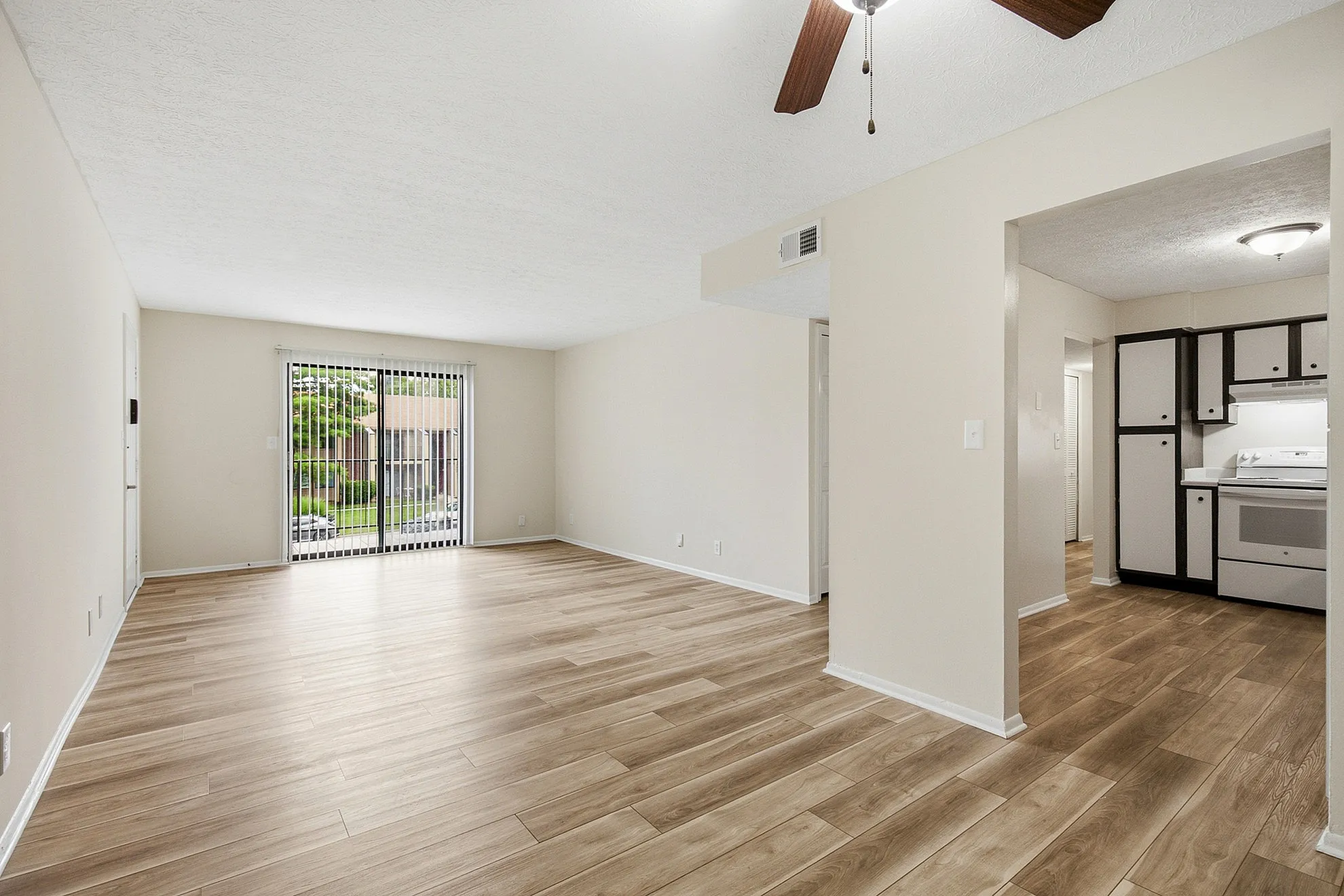 Bright and spacious living area with elegant wood flooring, large sliding glass doors, and a modern kitchen in a charming apartment.