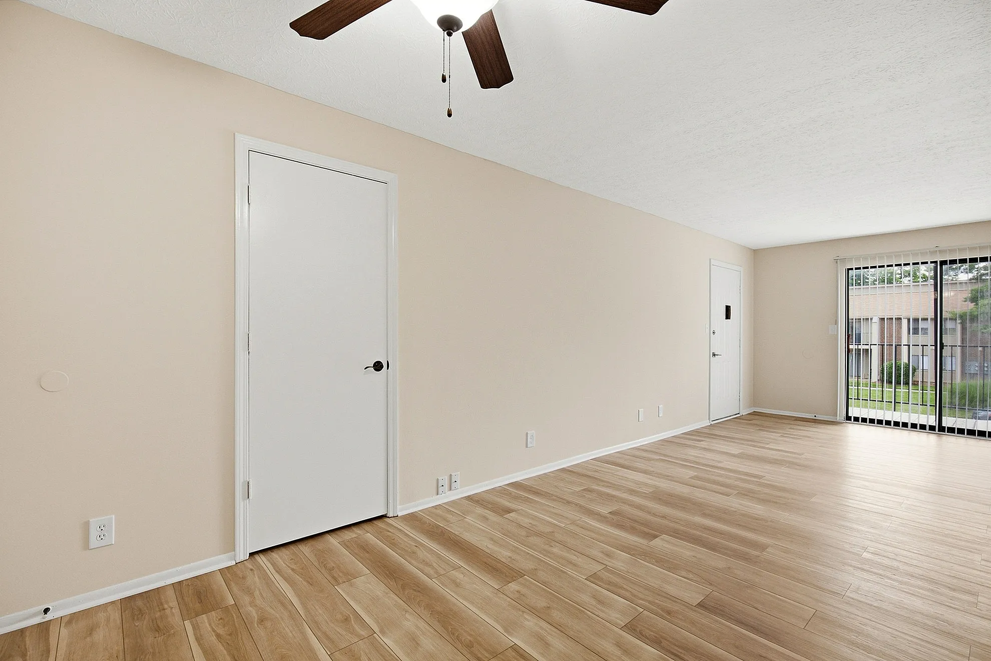 Bright and airy living room with modern wood flooring, ceiling fan, and large sliding glass doors leading to a scenic view.