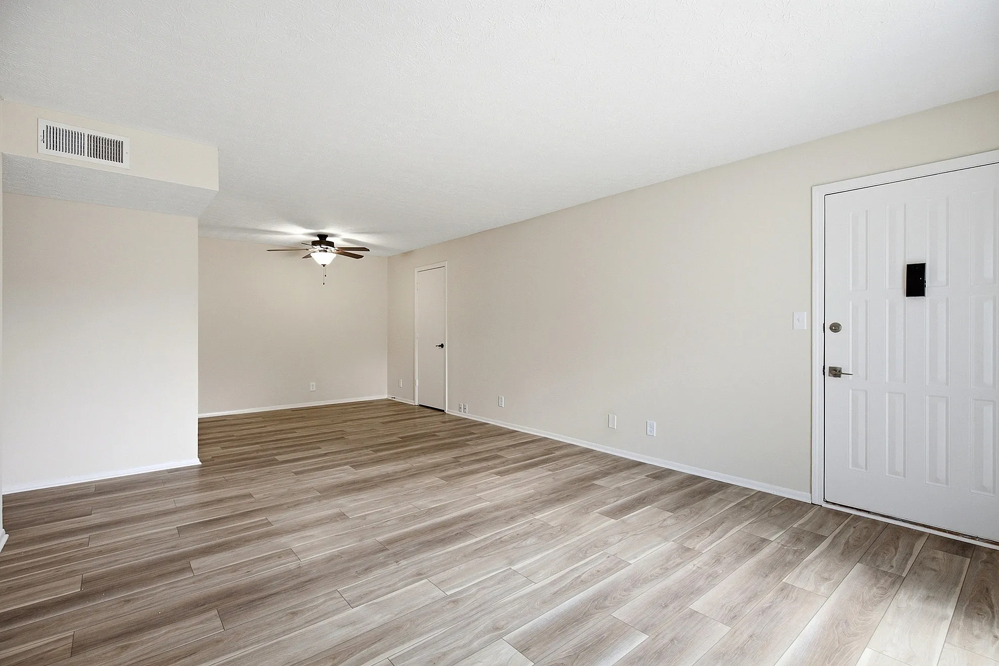 Bright and spacious living area with stylish wood flooring and modern ceiling fan, perfect for entertaining.
