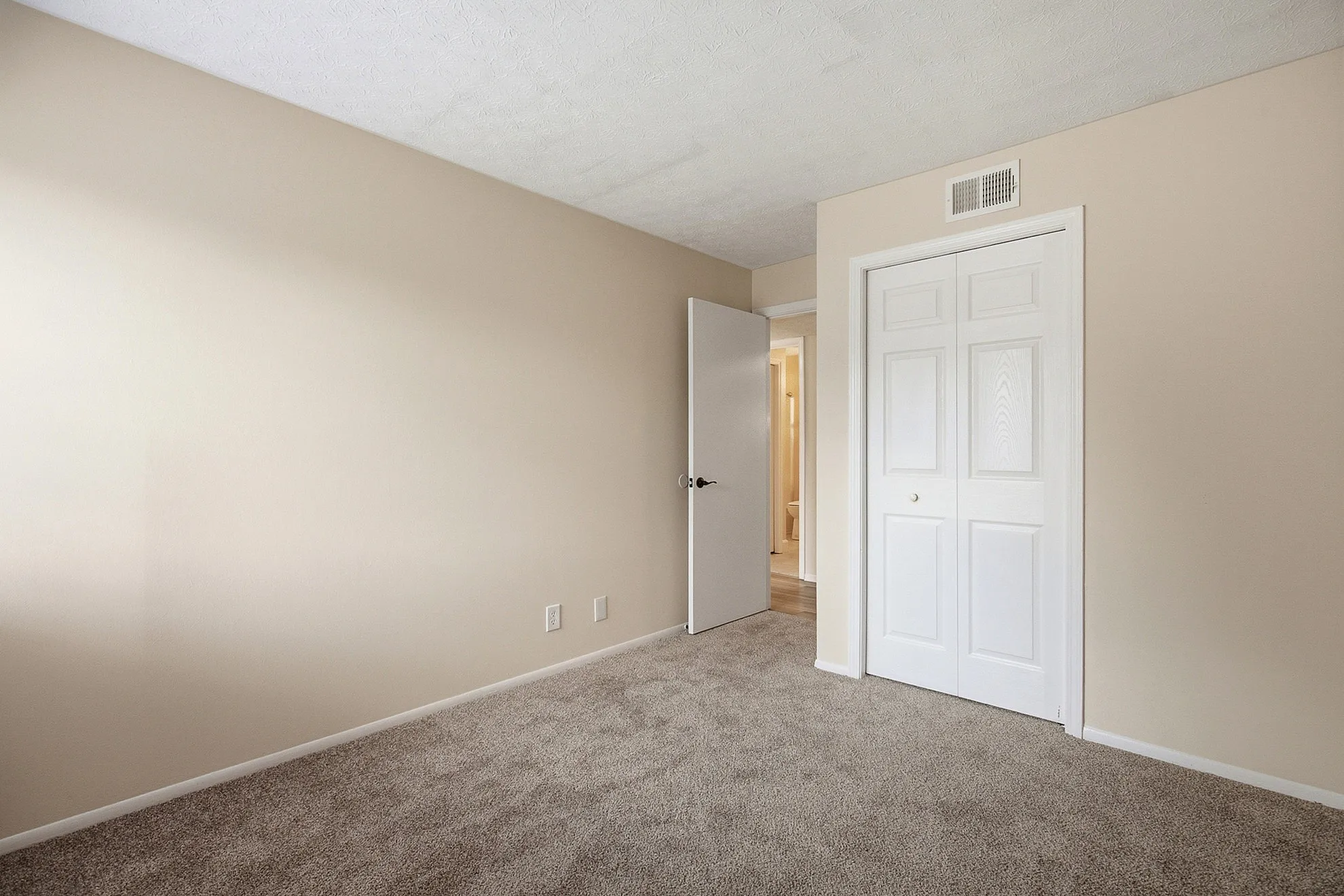 Inviting bedroom with plush carpeting, neutral walls, and ample closet space, perfect for creating a cozy retreat.