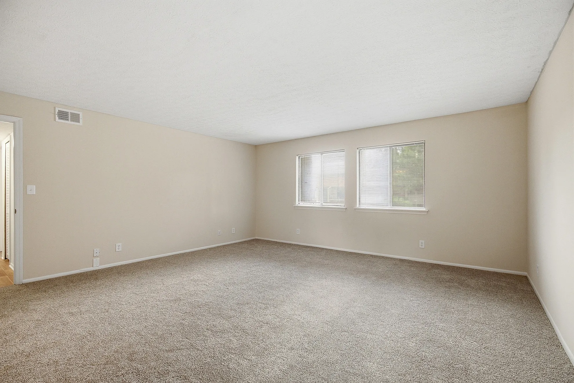 Spacious, sunlit room with plush carpeting and large windows, perfect for customization and comfort.