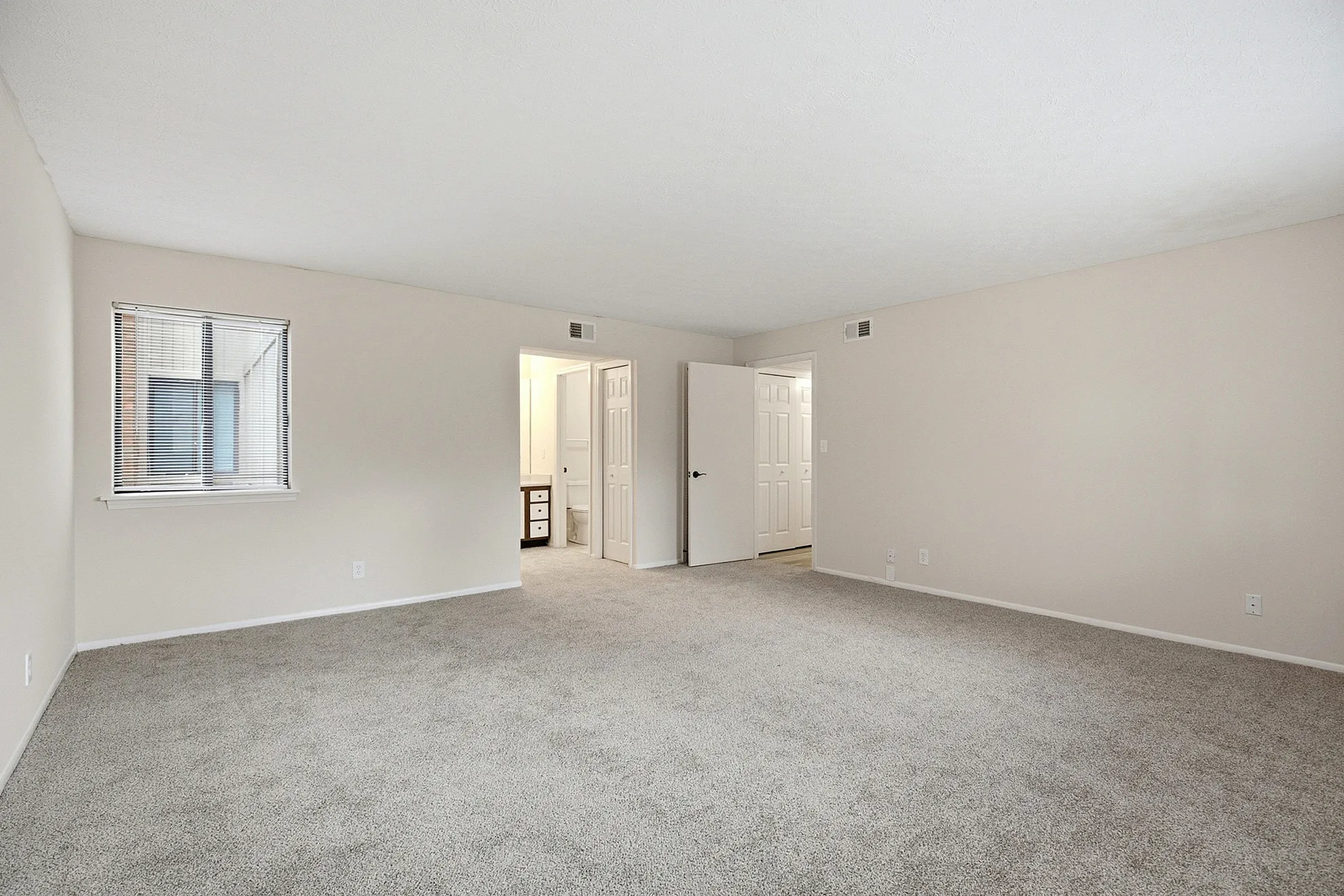 Bright and spacious room with plush carpeting, large window, and convenient access to an adjacent bathroom.