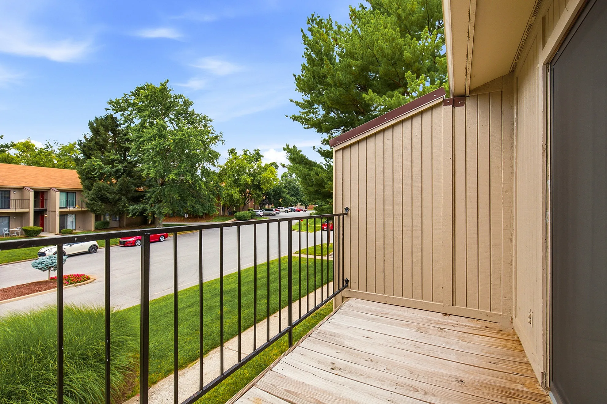 Charming apartment balcony with wooden deck overlooking a lush, tree-lined street view.