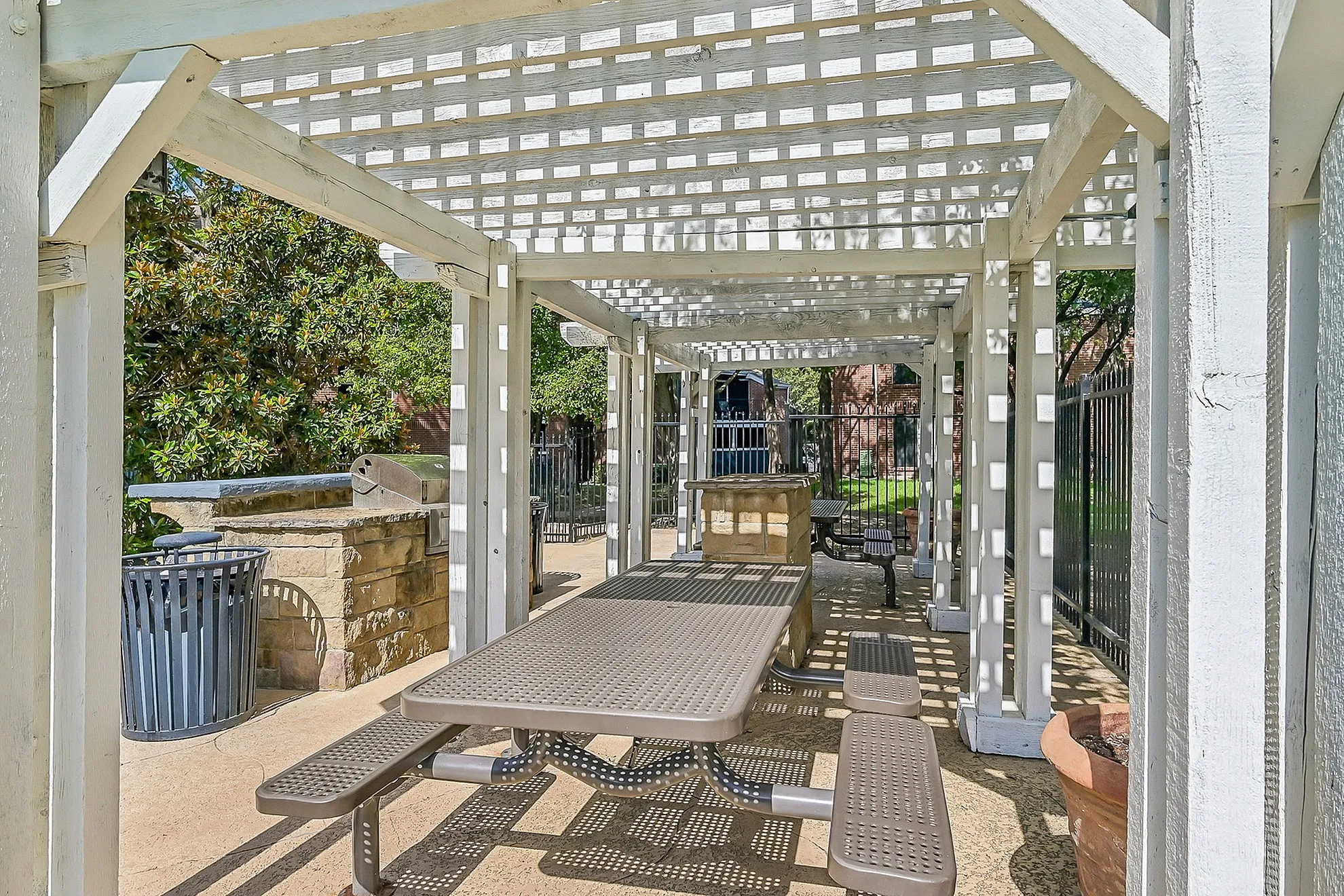 Charming outdoor pergola with picnic tables and built-in grill, perfect for entertaining in a lush, sunny setting.