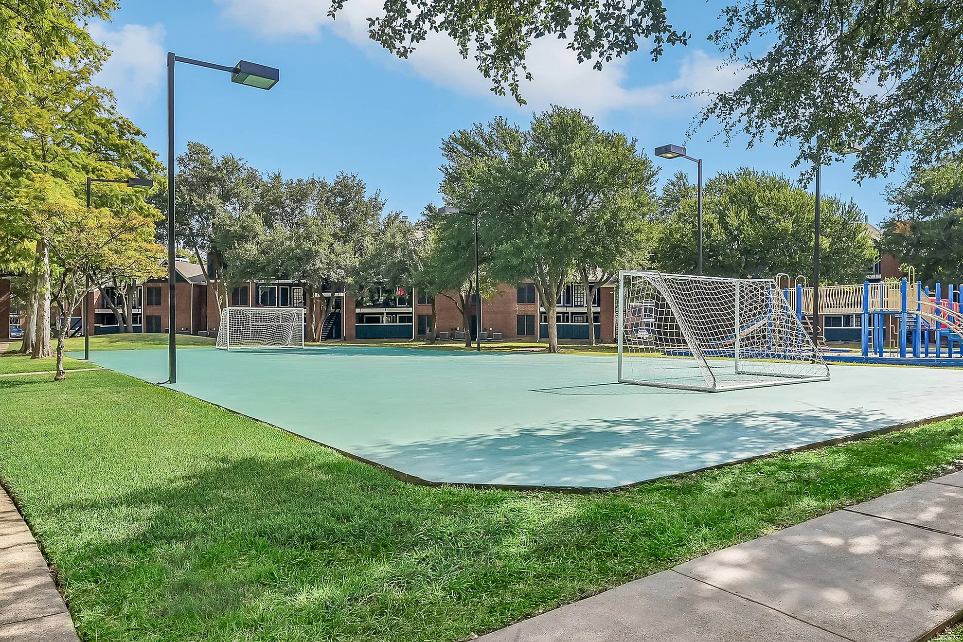 Charming outdoor recreational area featuring a multi-sport court with soccer goals, surrounded by lush greenery and a modern playground, perfect for active living in a vibrant community.