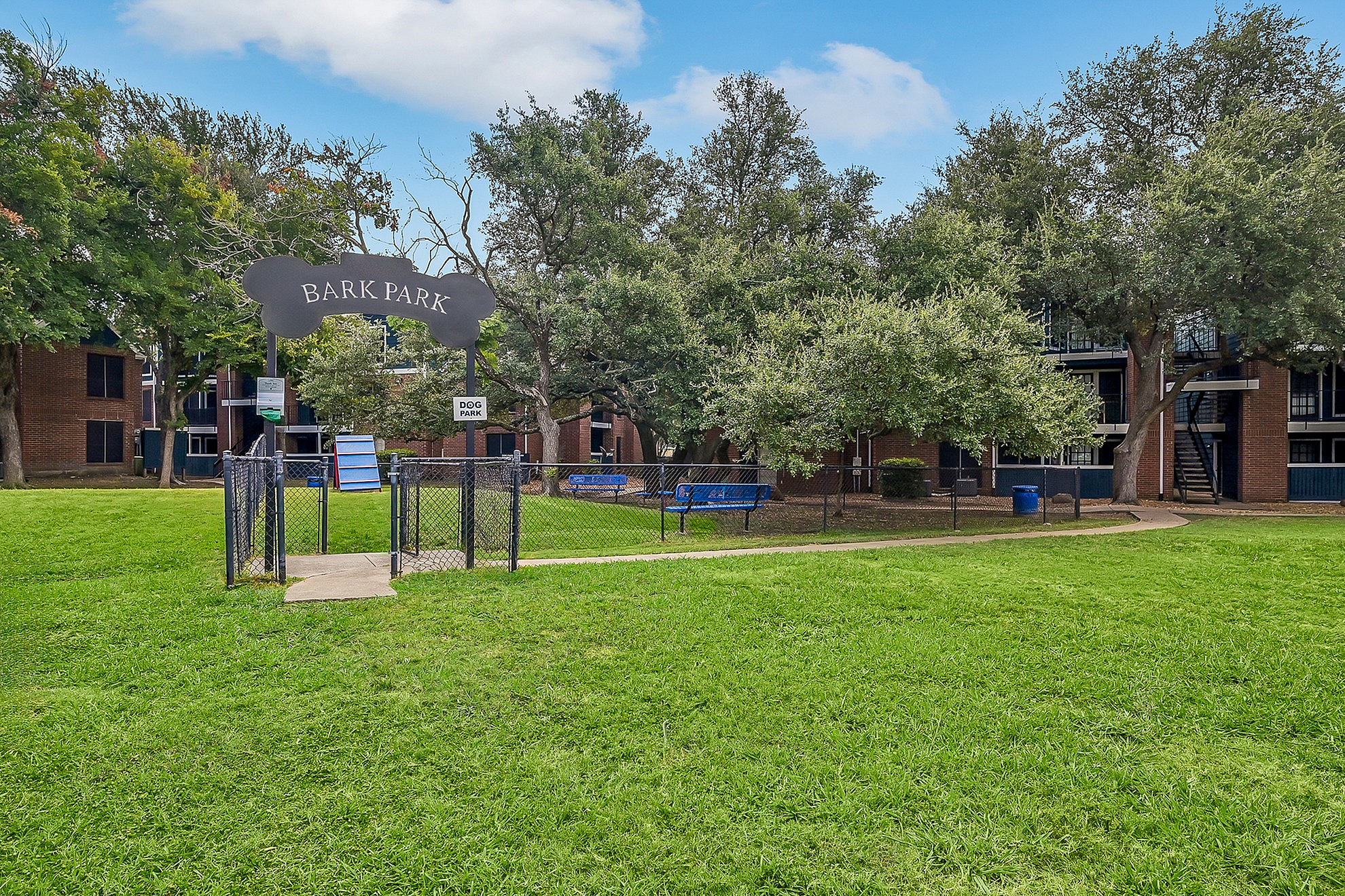 Inviting community dog park surrounded by lush greenery and modern brick apartments.