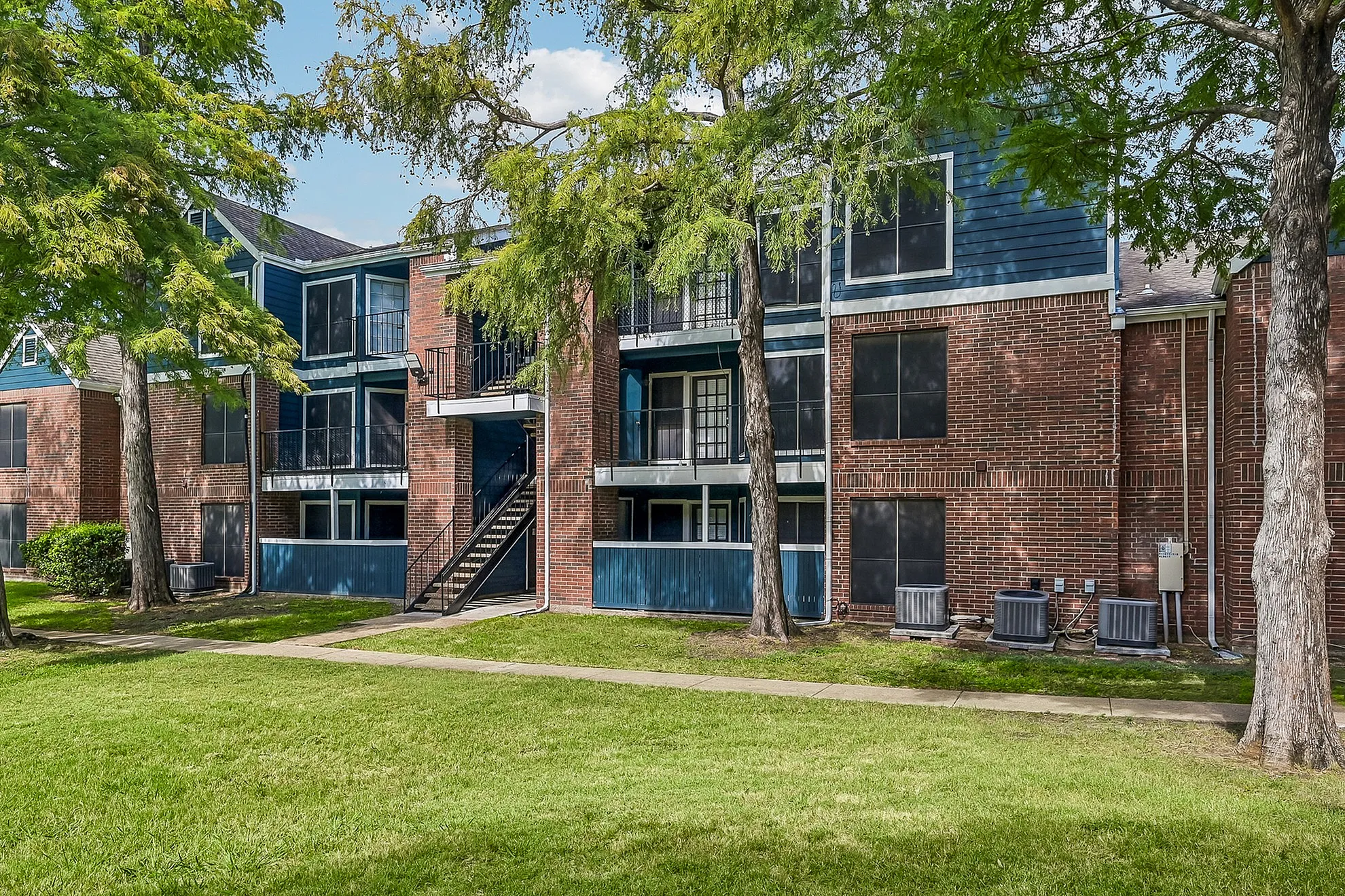 Charming apartment complex with brick facade and lush green landscaping, offering a tranquil living environment.