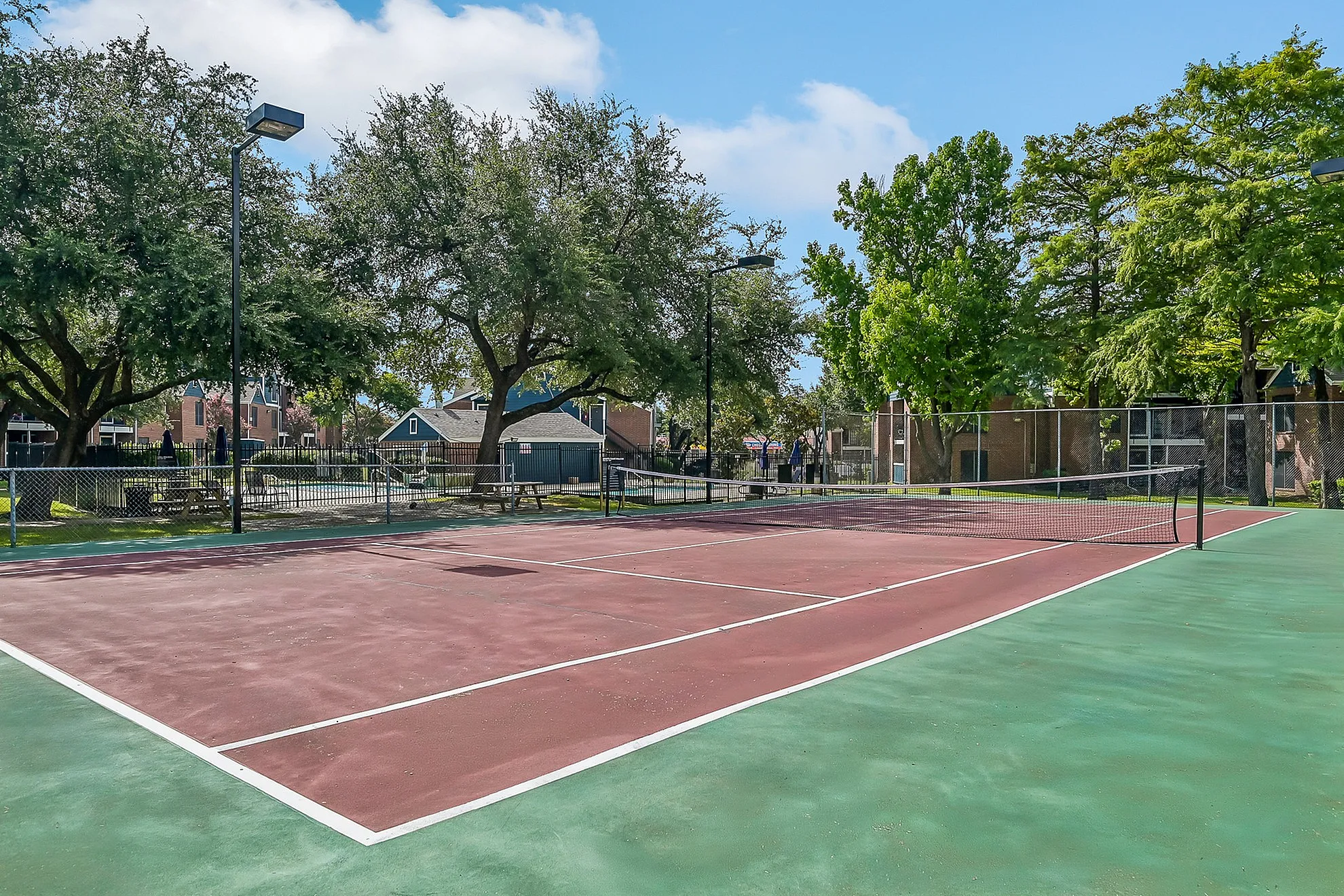Vibrant tennis court nestled in a serene residential area, surrounded by lush trees and inviting community spaces.