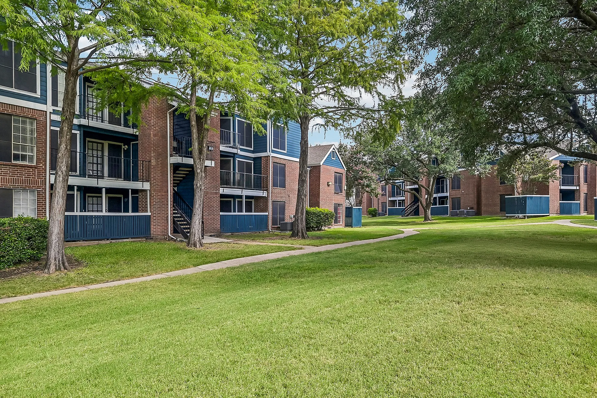 Charming apartment complex surrounded by lush greenery, with spacious balconies and modern brick design.