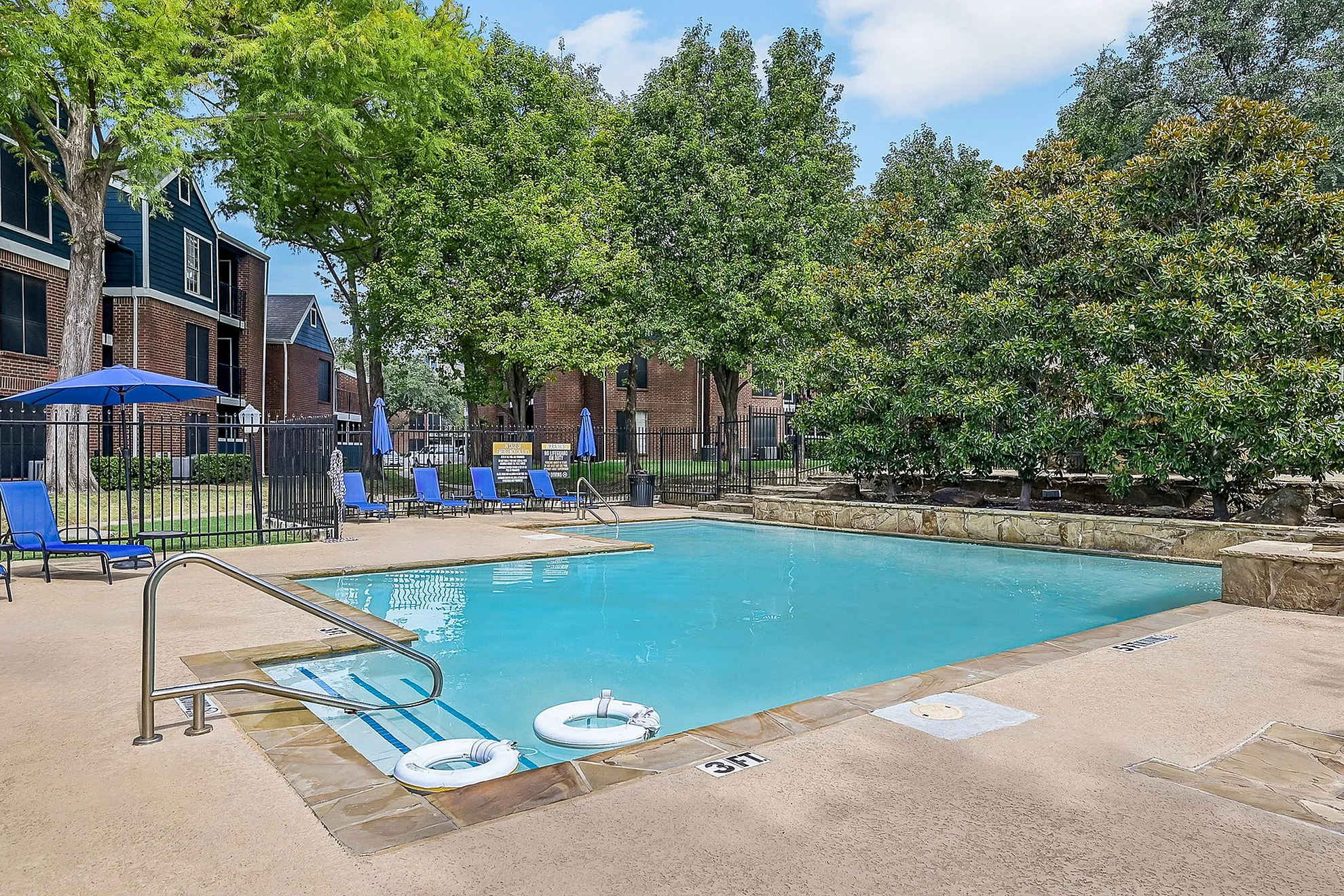 Inviting outdoor pool area with stylish deck chairs and vibrant blue umbrellas set amongst lush greenery, ideal for relaxation and leisure.