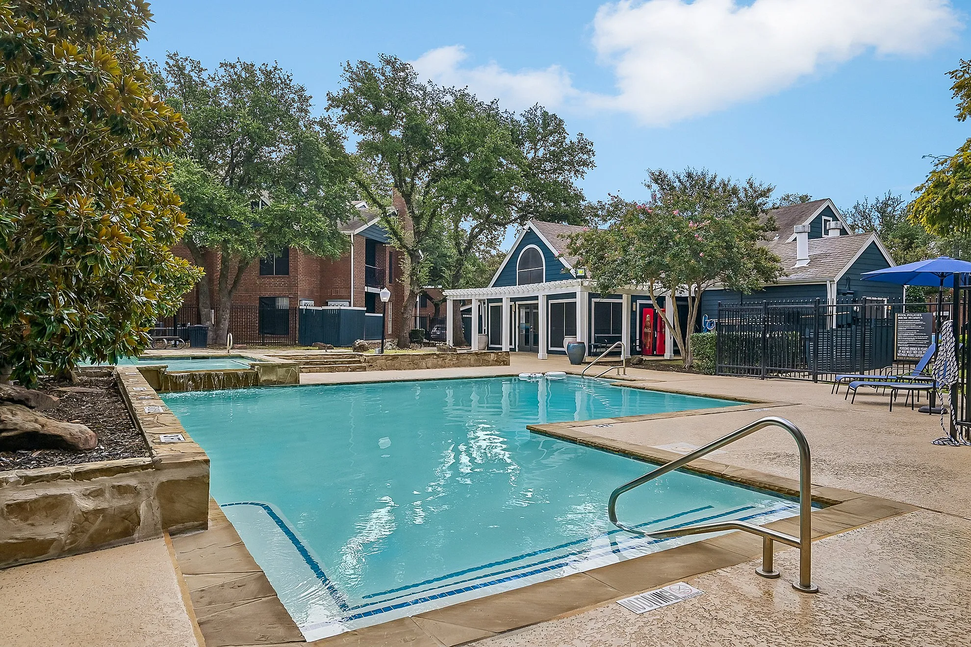 Inviting apartment community pool area surrounded by lush greenery and charming buildings, perfect for relaxation and leisure.