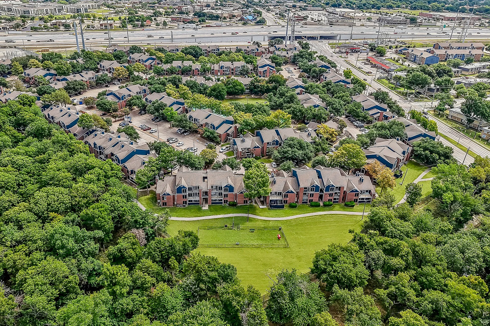 Scenic aerial view of charming apartment community surrounded by lush greenery with easy freeway access.