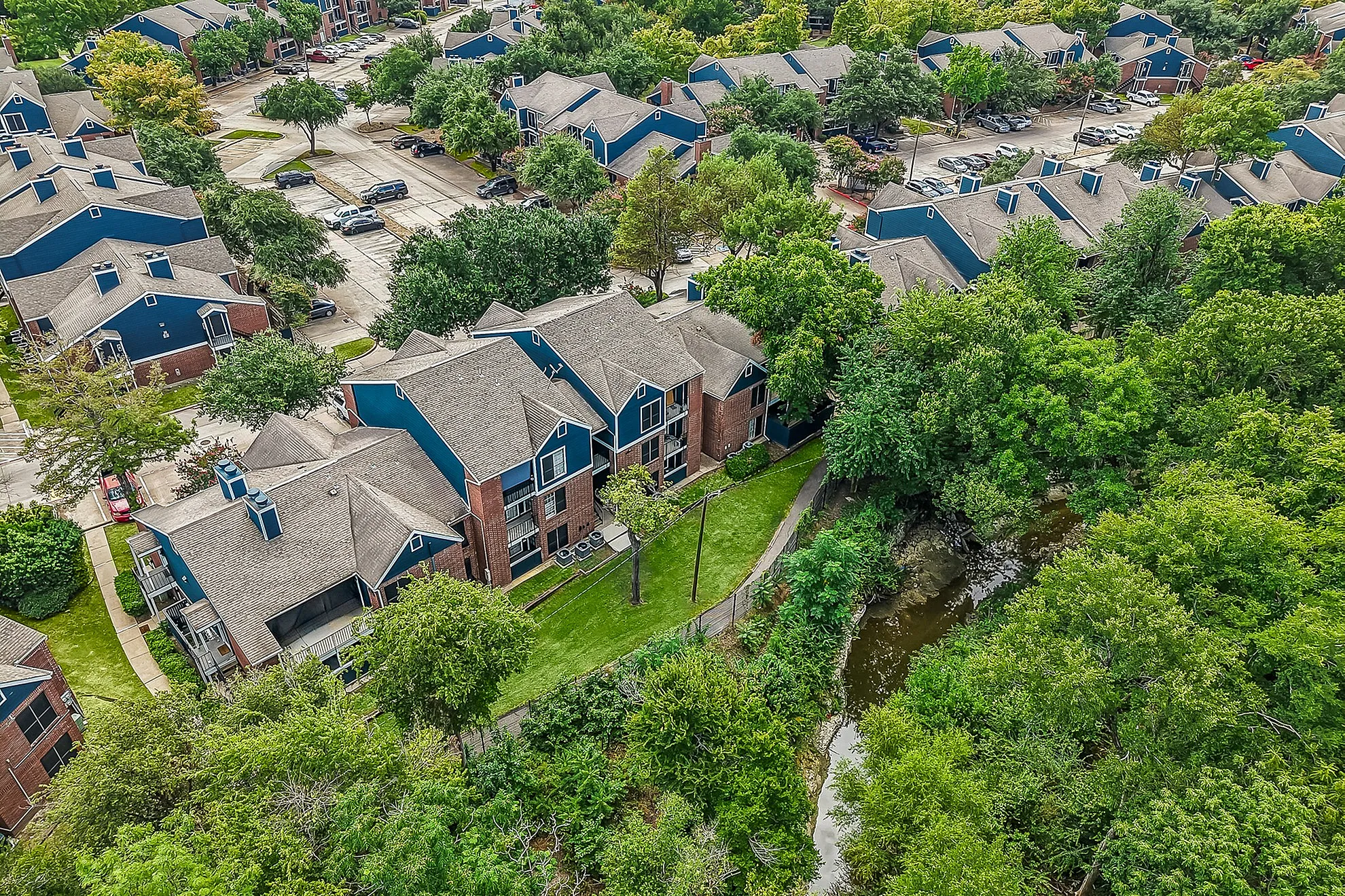 Charming aerial view of modern apartment complex surrounded by lush greenery and a serene creek.