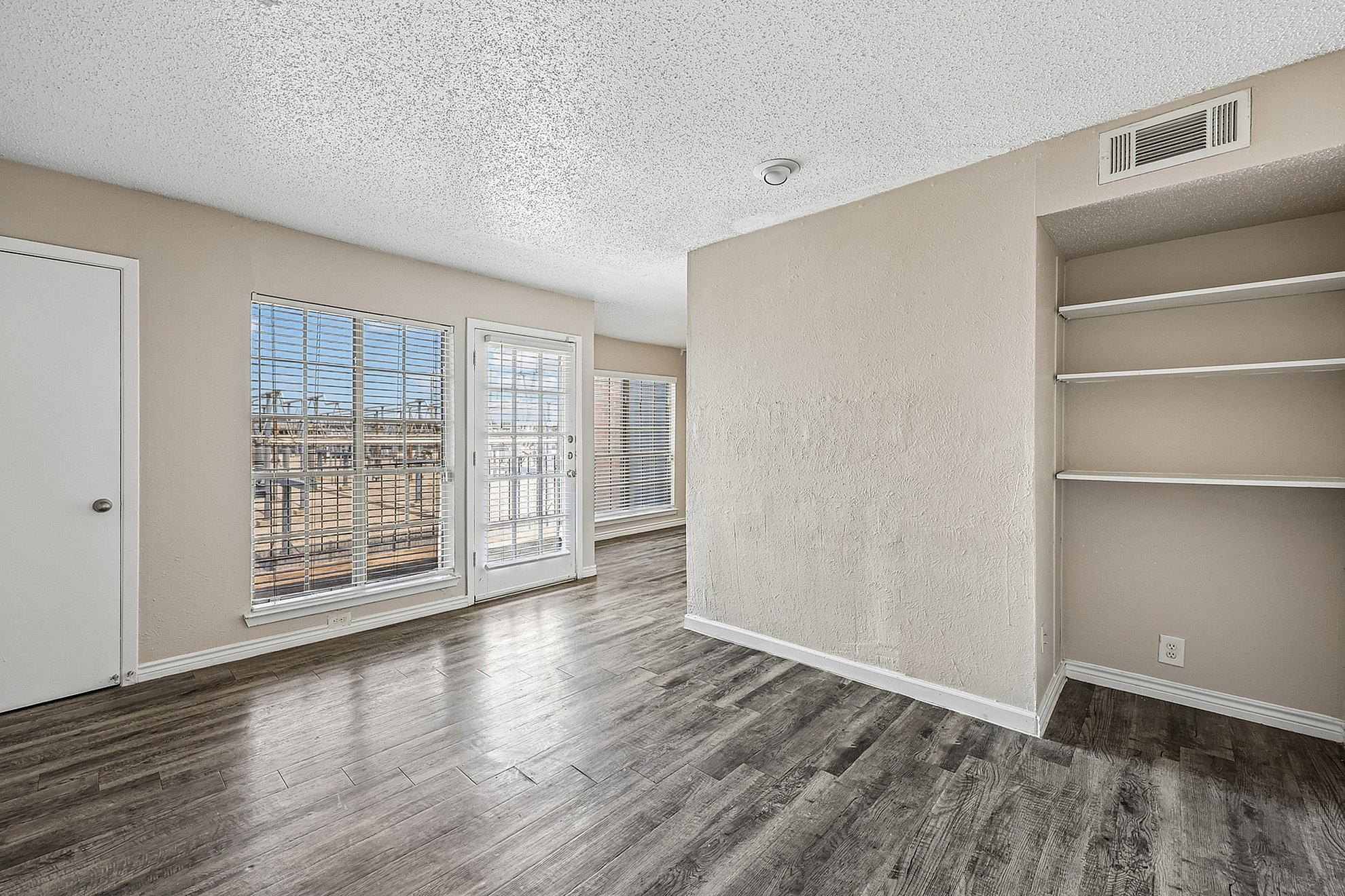 Bright and airy apartment space featuring large windows, elegant wooden flooring, and built-in shelving for modern living.