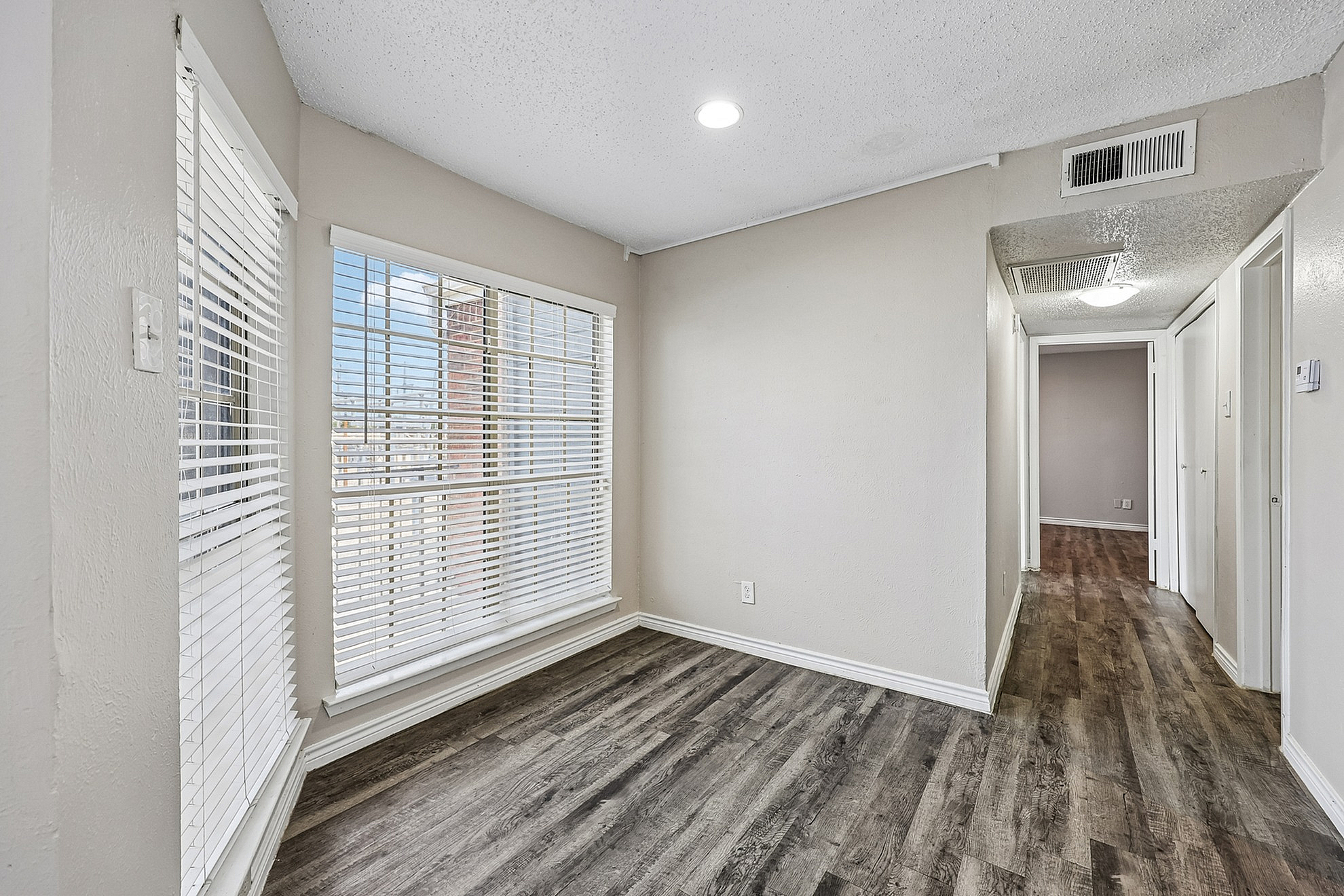 Bright hallway with stylish wood flooring and large windows featuring modern blinds, creating an inviting atmosphere.