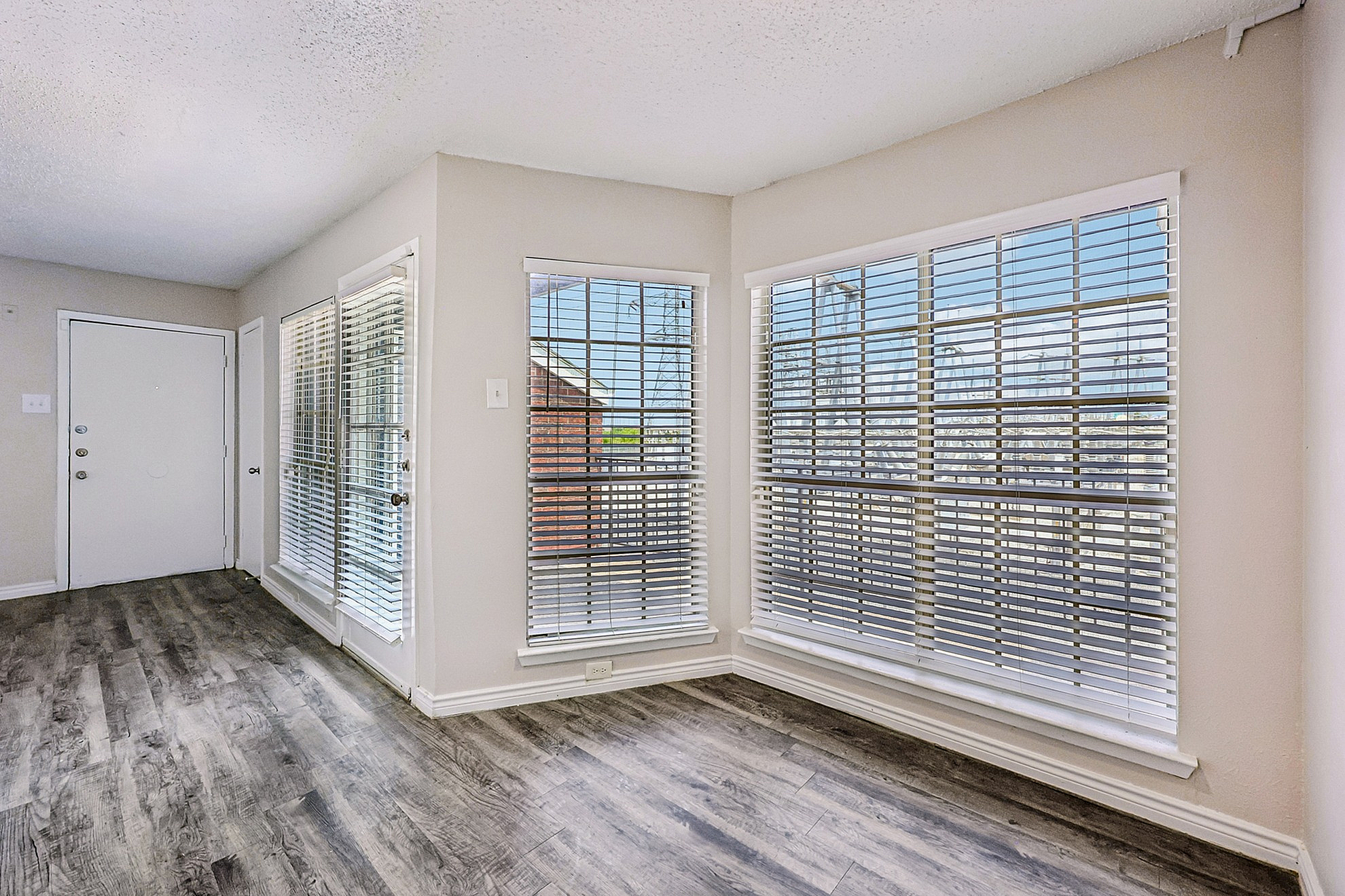 Bright and welcoming apartment with large windows and stylish wood flooring, offering ample natural light and inviting ambience.