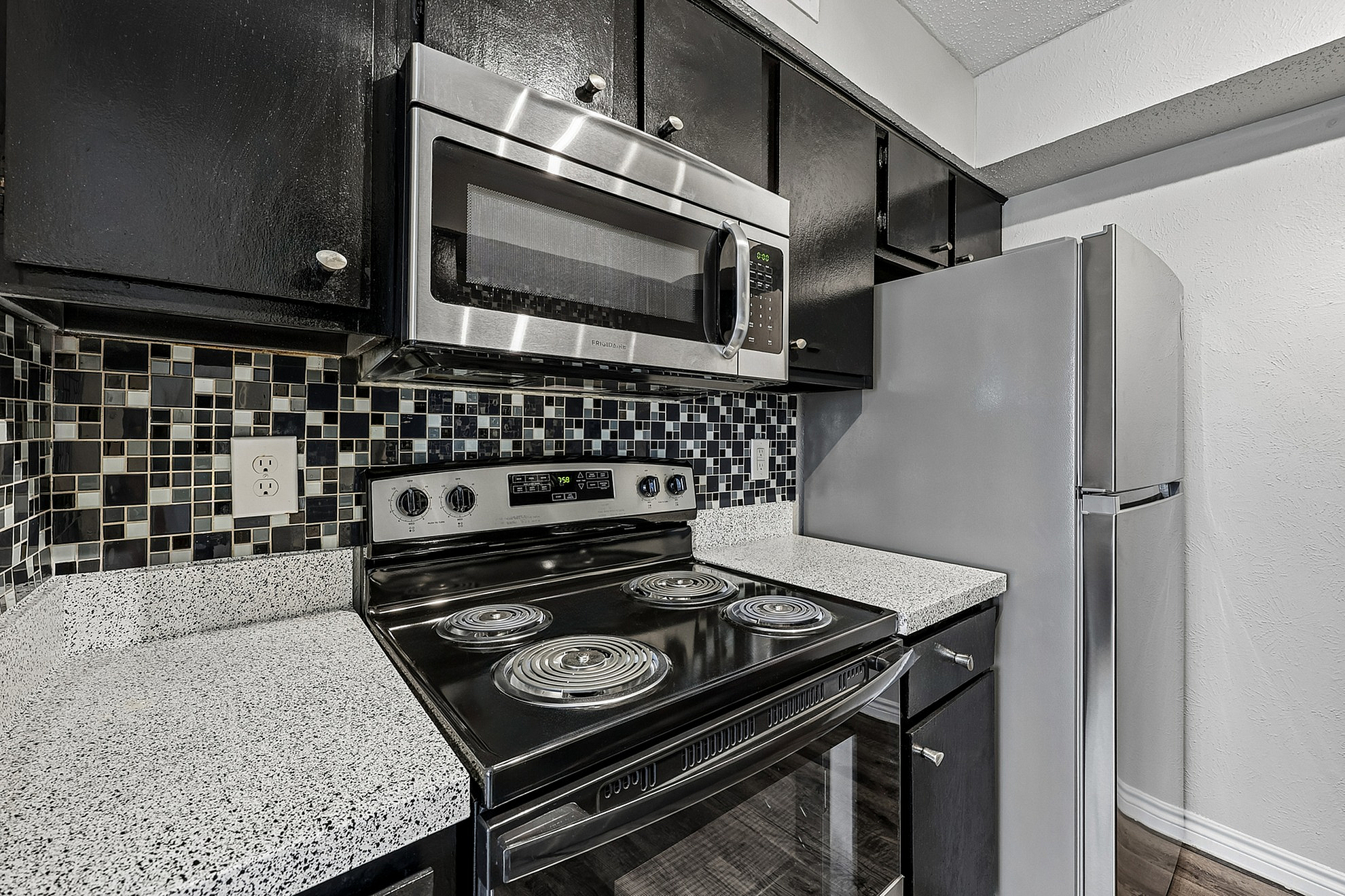 Modern kitchen with sleek stainless steel appliances, elegant black cabinetry, and stylish mosaic tile backsplash.