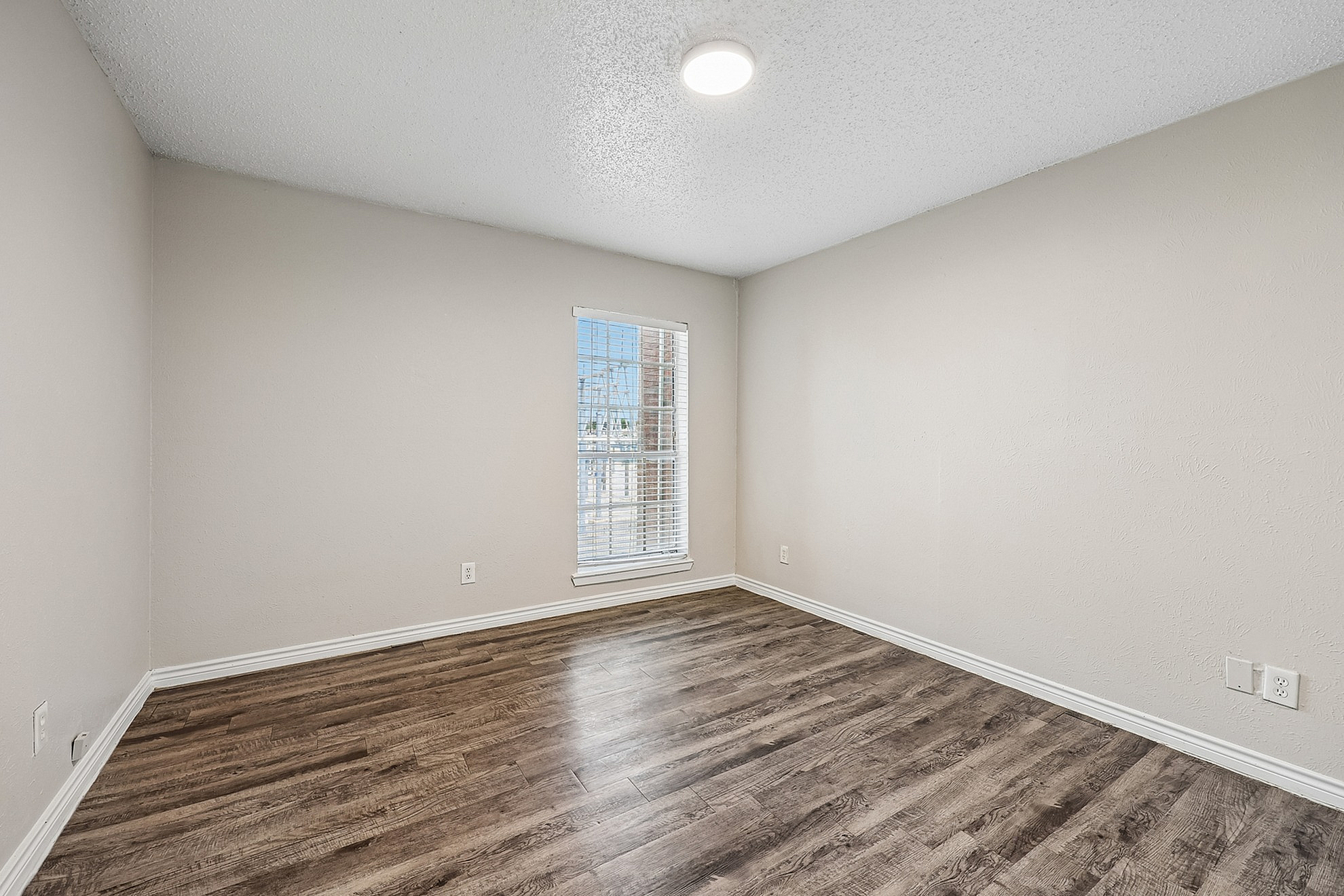 Inviting room with elegant wood flooring and bright window, offering abundant natural light and a fresh, modern feel.