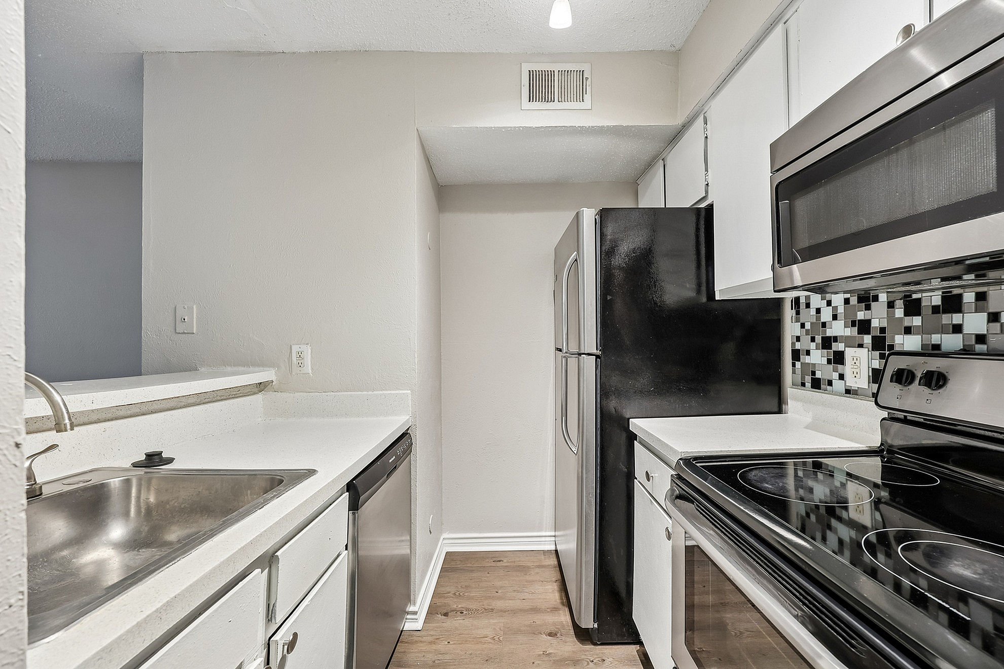 Modern kitchen with sleek stainless-steel appliances, pristine white countertops, and stylish mosaic backsplash, ideal for culinary enthusiasts.