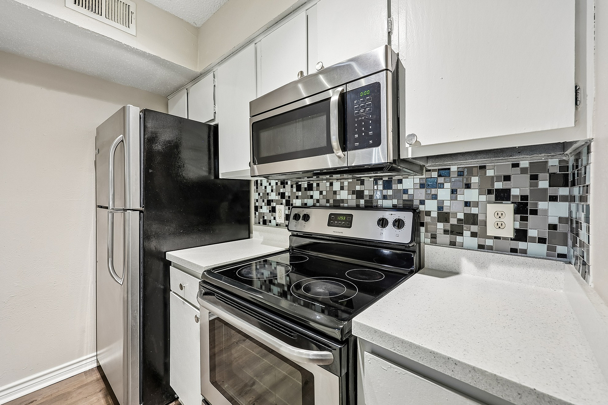 Modern kitchen featuring sleek stainless steel appliances, elegant mosaic tile backsplash, and pristine white countertops.