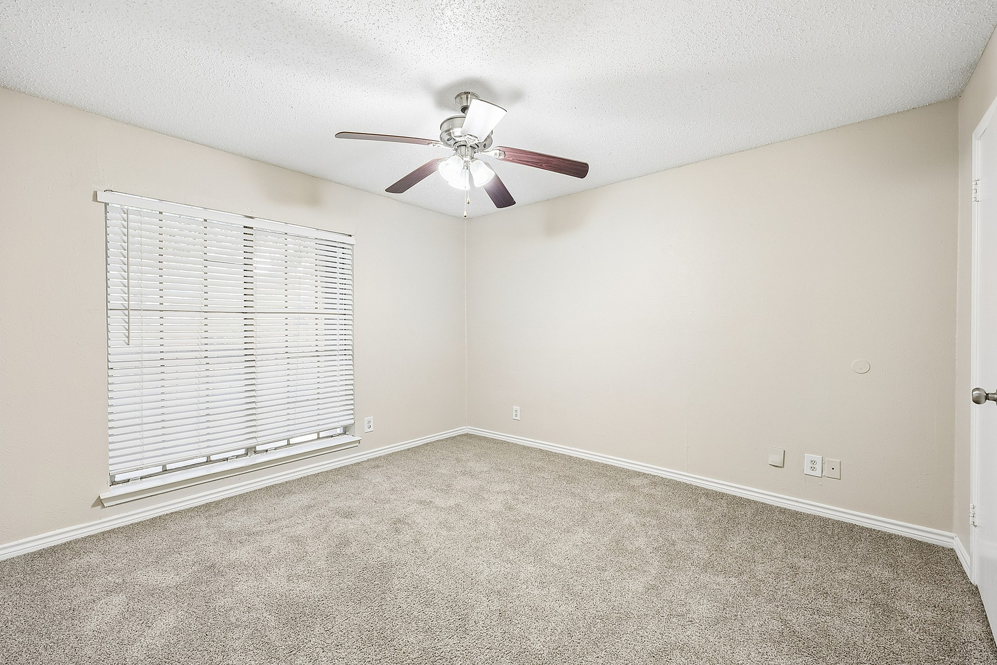 Bright and airy bedroom with plush carpeting, a modern ceiling fan, and large window with blinds for ample natural light.