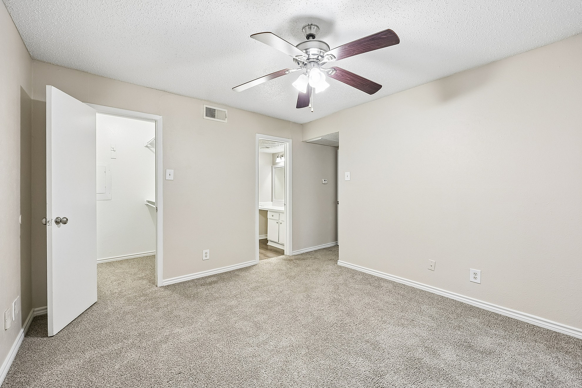 Bright and spacious bedroom with modern ceiling fan, cozy carpet, and convenient walk-in closet entrance.