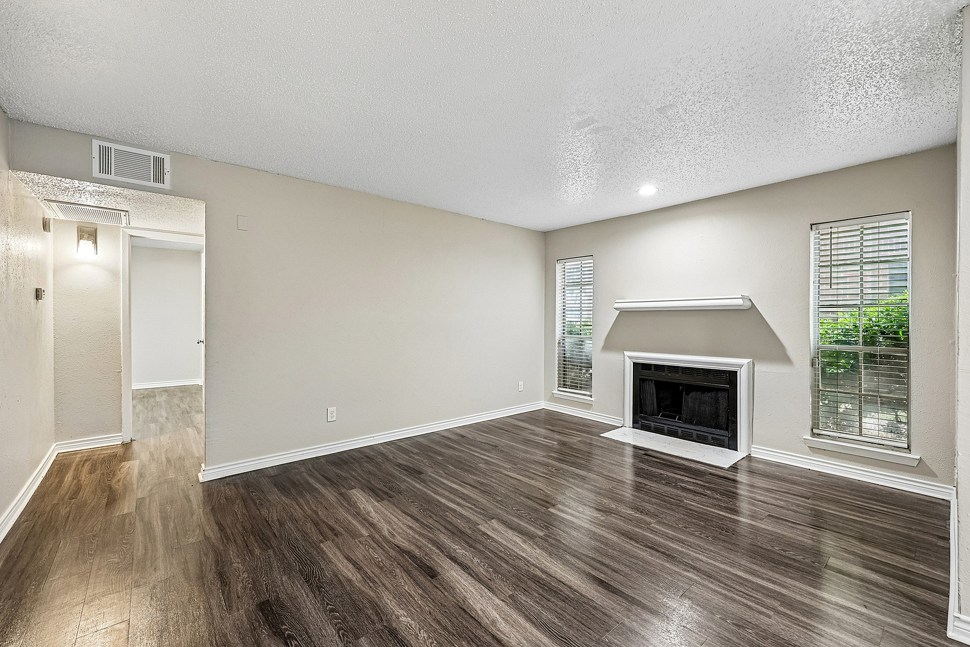 Inviting living room with elegant dark wood flooring, cozy fireplace, and ample natural light from large windows.