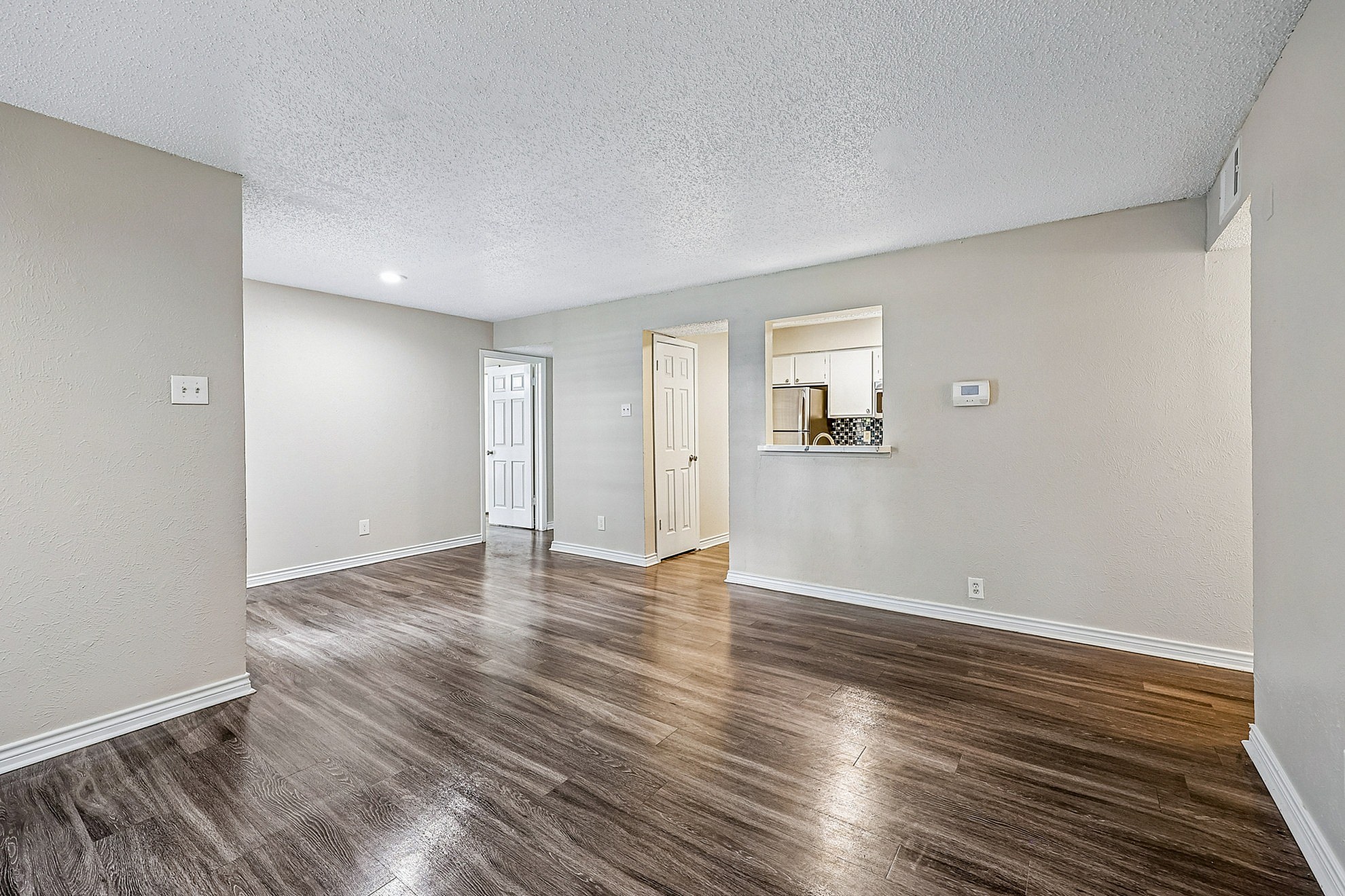Spacious living area with elegant wood flooring, neutral walls, and a view into the modern kitchen featuring a stylish backsplash.