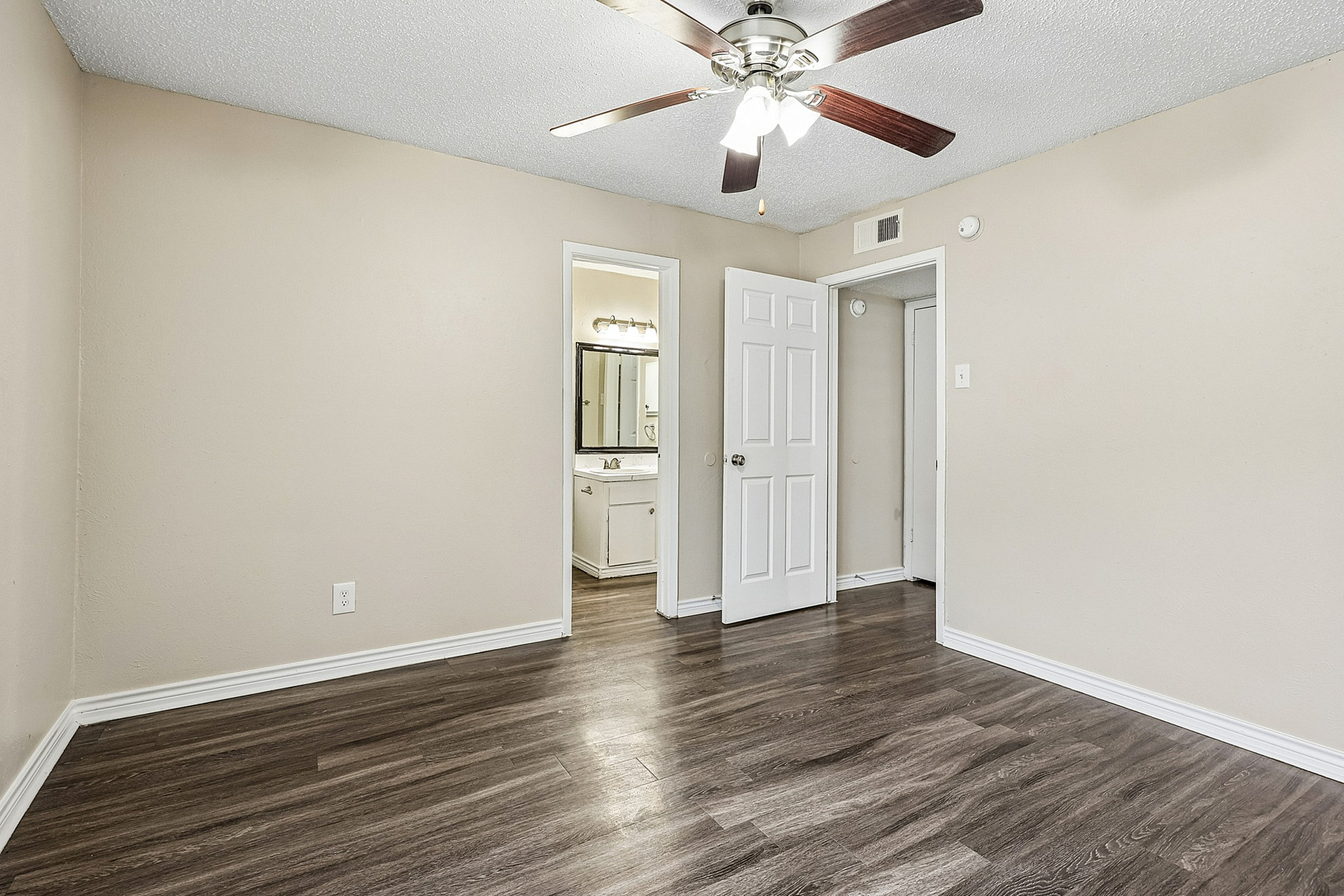 Bright and inviting bedroom with elegant hardwood flooring and modern ceiling fan, leading to a private en-suite bath.