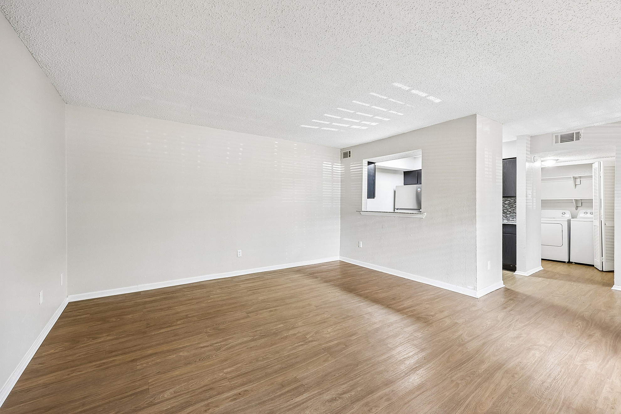 Bright and spacious living area with sleek wooden flooring, an open pass-through to a modern kitchen, and convenient in-unit laundry facilities.