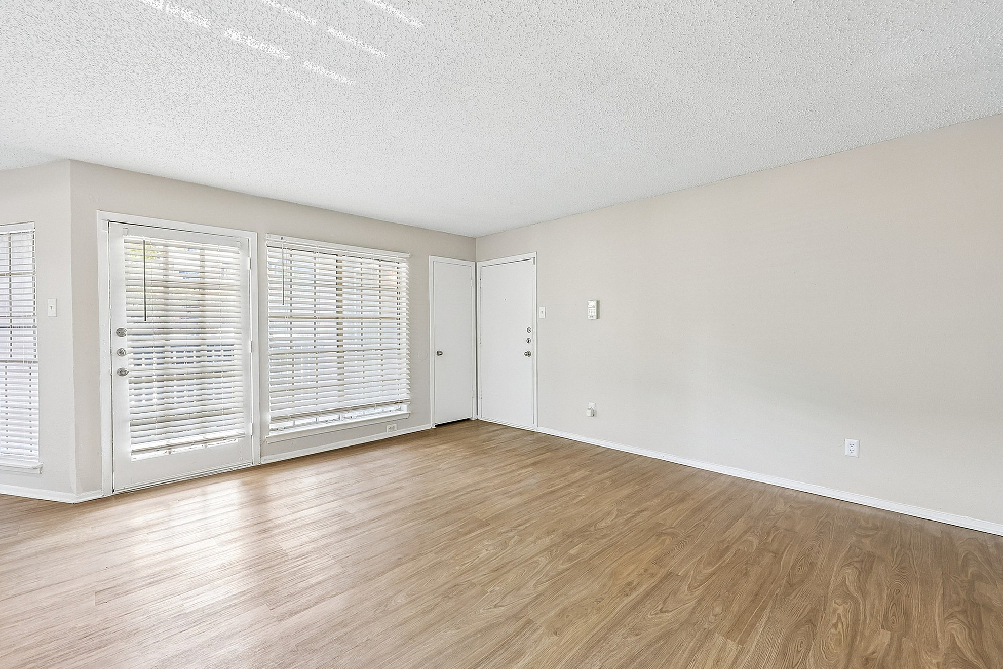 Bright and airy living room with large windows, elegant wooden flooring, and fresh white walls, perfect for cozy relaxation.