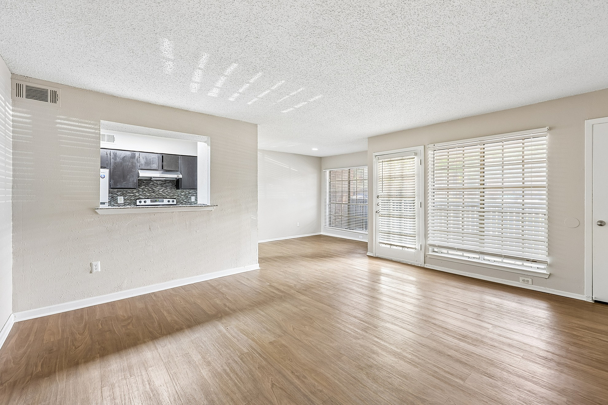 Bright open-plan living area with stylish wooden flooring and ample natural light, connected to a modern kitchen with sleek finishes.