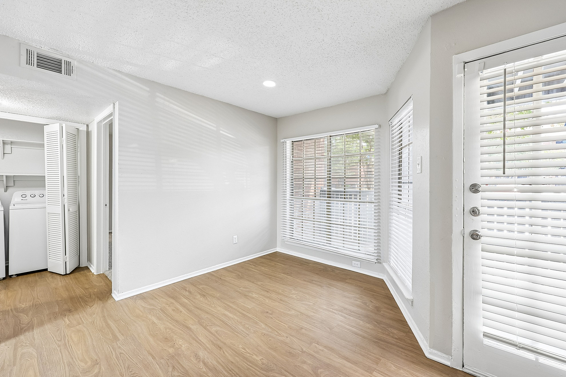 Bright, airy room with elegant wood flooring, large windows, and an abundance of natural light, offering a fresh and inviting ambiance.