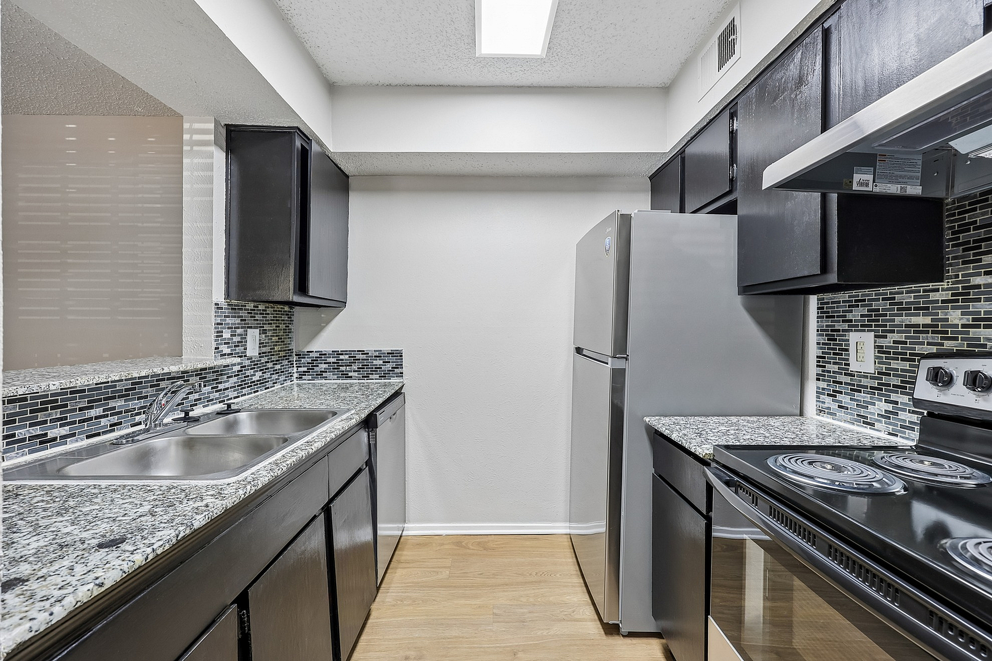 Modern kitchen with sleek black cabinetry, stainless steel appliances, and stylish tile backsplash.