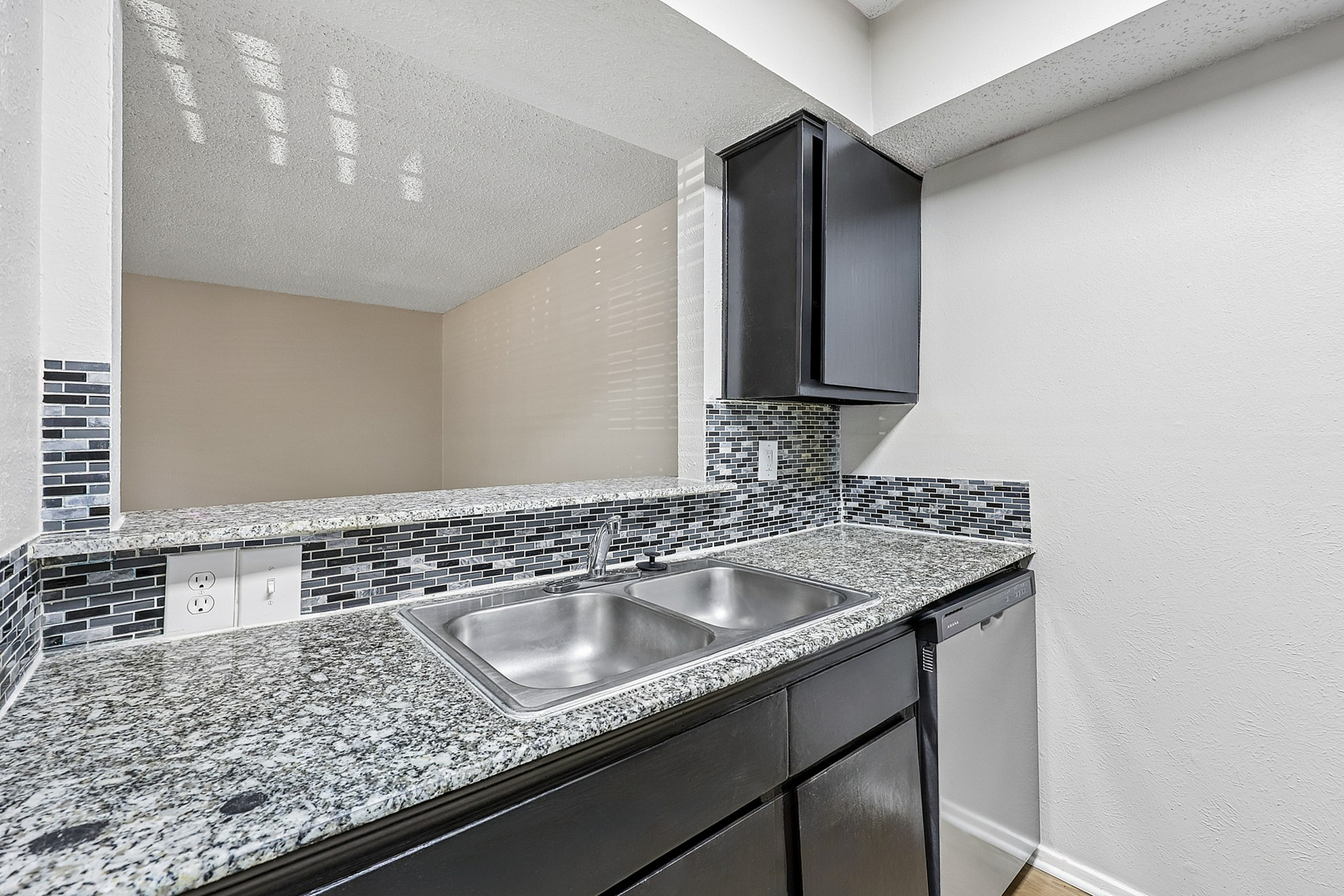 Modern kitchen area featuring sleek granite countertops, stylish mosaic backsplash, and elegant dark cabinetry with a stainless steel sink.