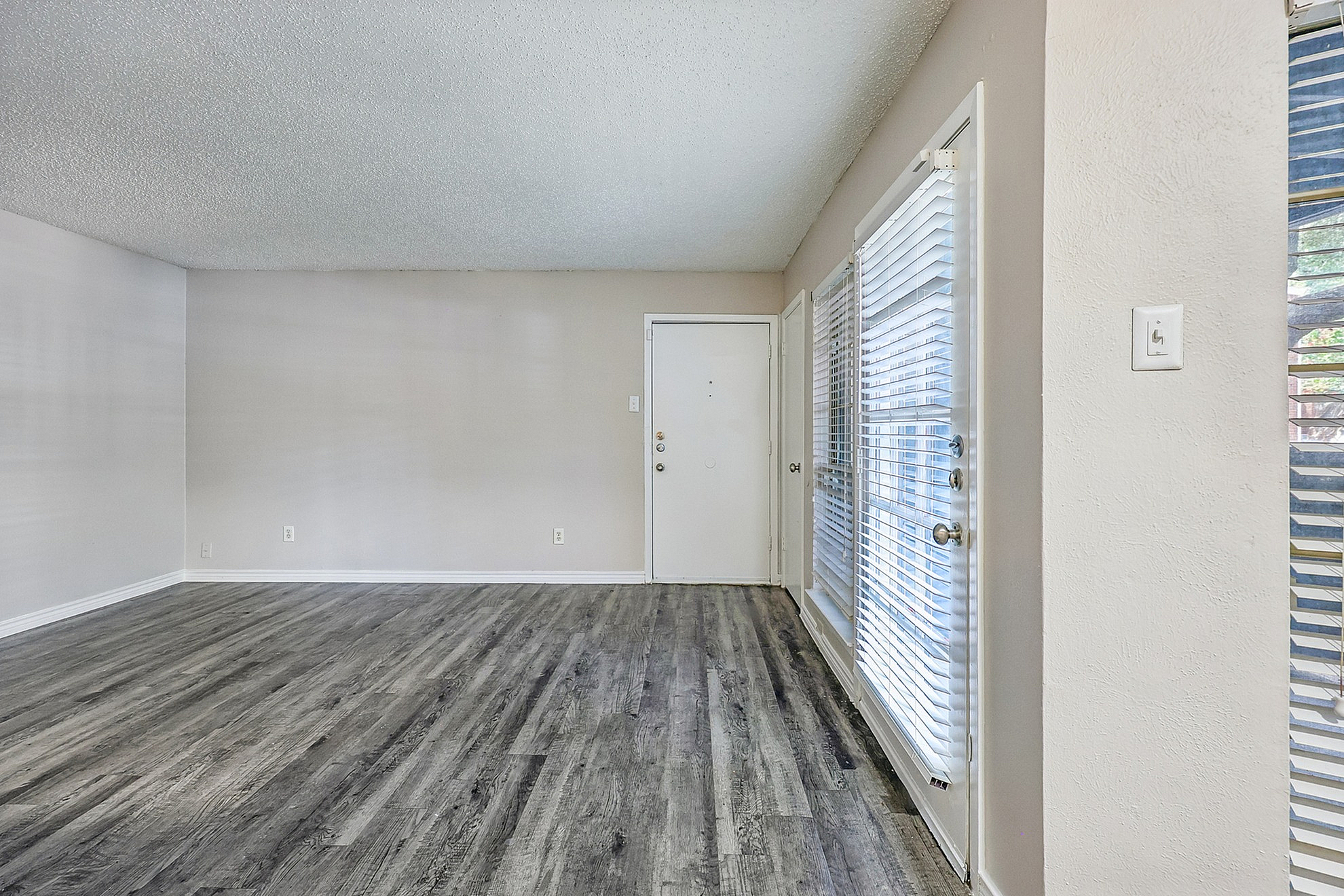 Bright and spacious living room with modern wood flooring and large windows with blinds for natural light.