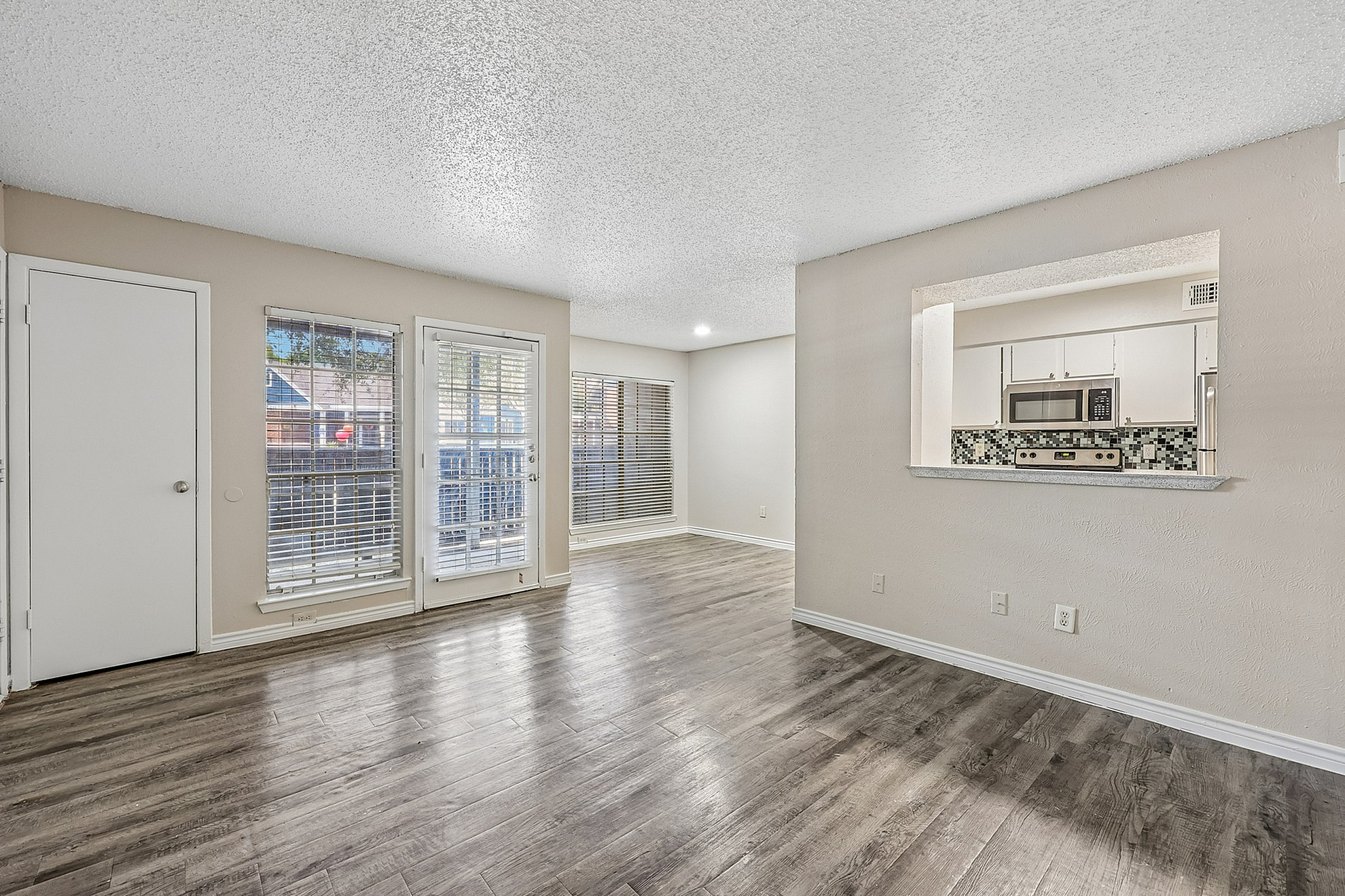 Bright and spacious living area with elegant wood floors, ample natural light, and a modern kitchen pass-through.