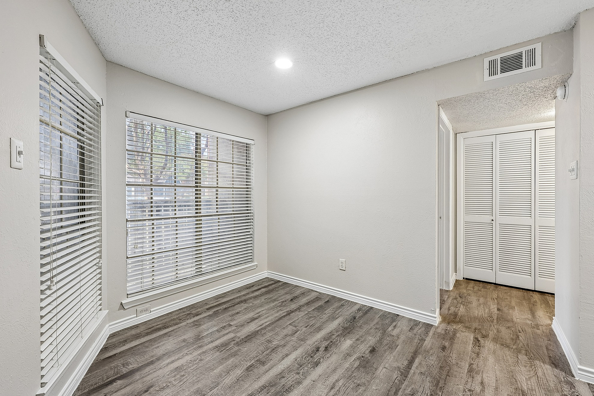 Bright, modern apartment corner with large windows, sleek blinds, and elegant wood flooring, offering a cozy and inviting atmosphere.