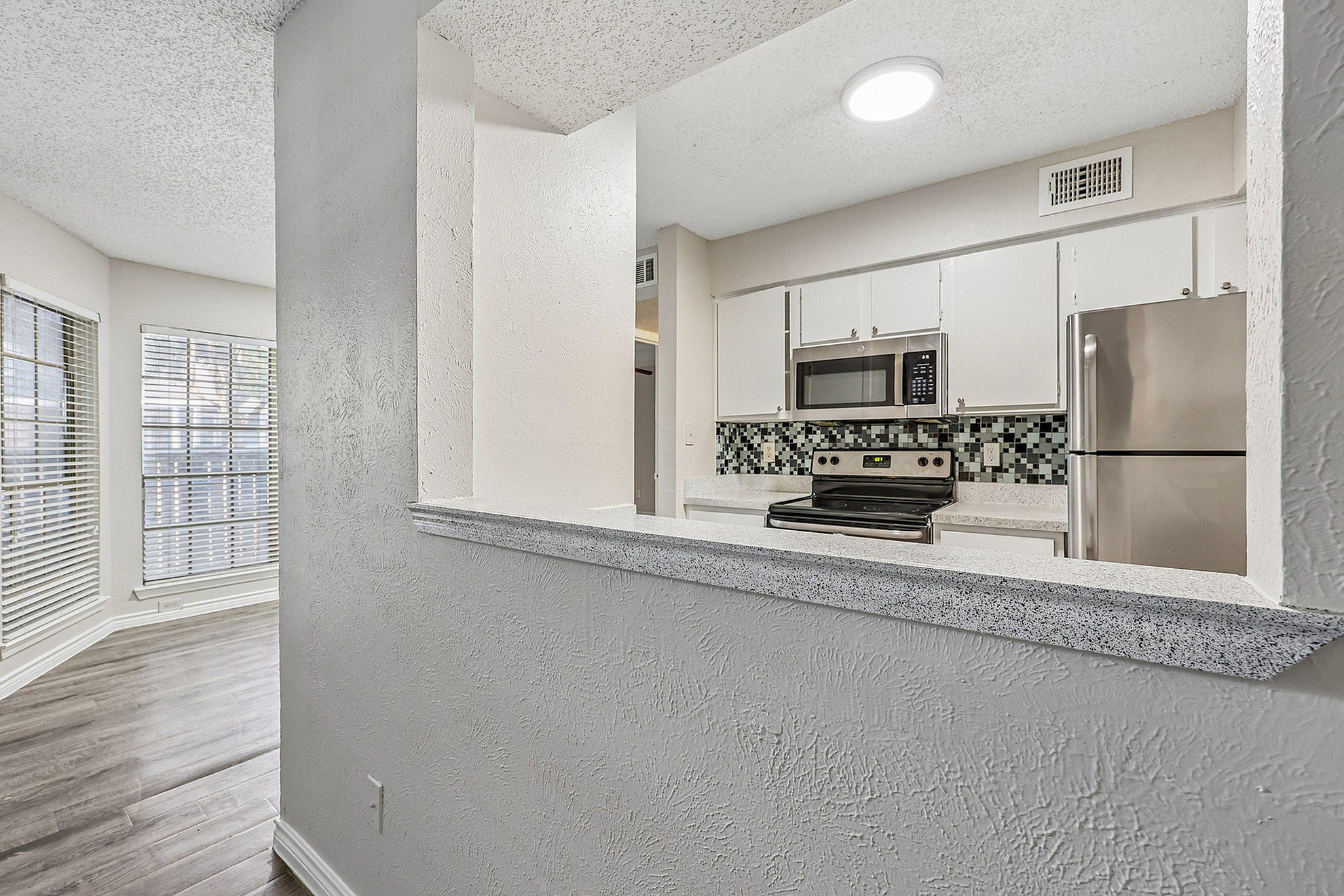 Inviting open kitchen with modern stainless steel appliances and chic tile backsplash, seamlessly connected to a sunlit living area with elegant hardwood floors.