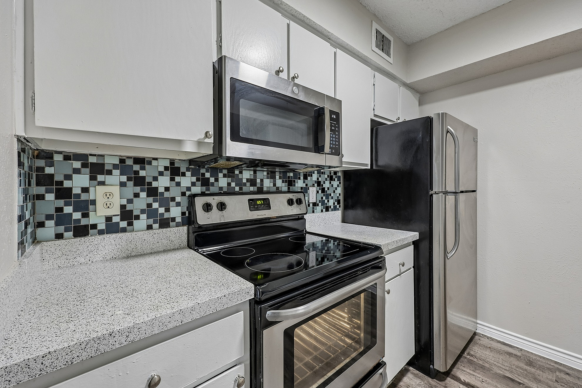Charming modern kitchen with sleek stainless steel appliances, elegant speckled countertops, and a stylish mosaic tile backsplash.