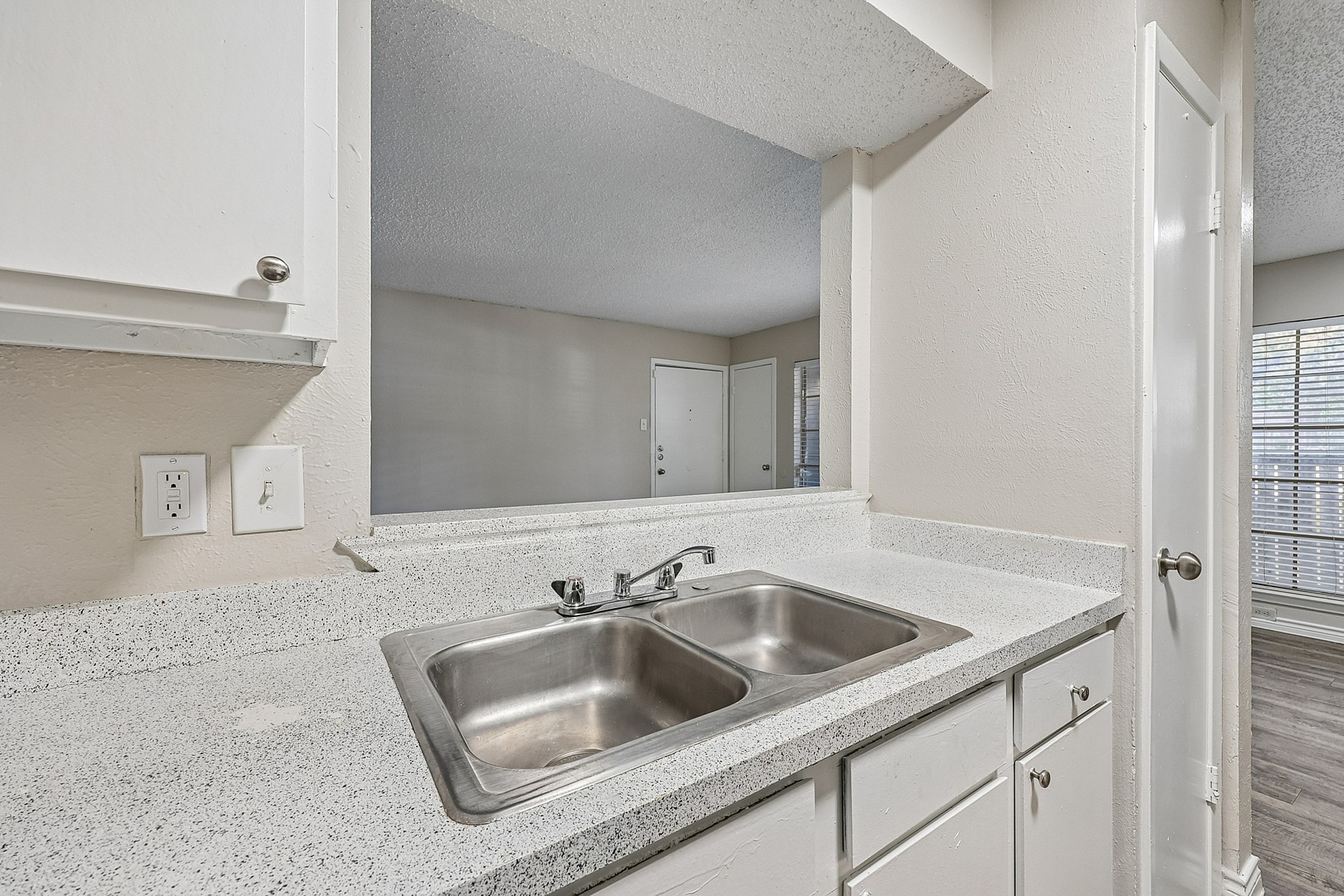 Bright and inviting kitchen with a sleek dual sink, modern countertops, and view into a sunlit living area.